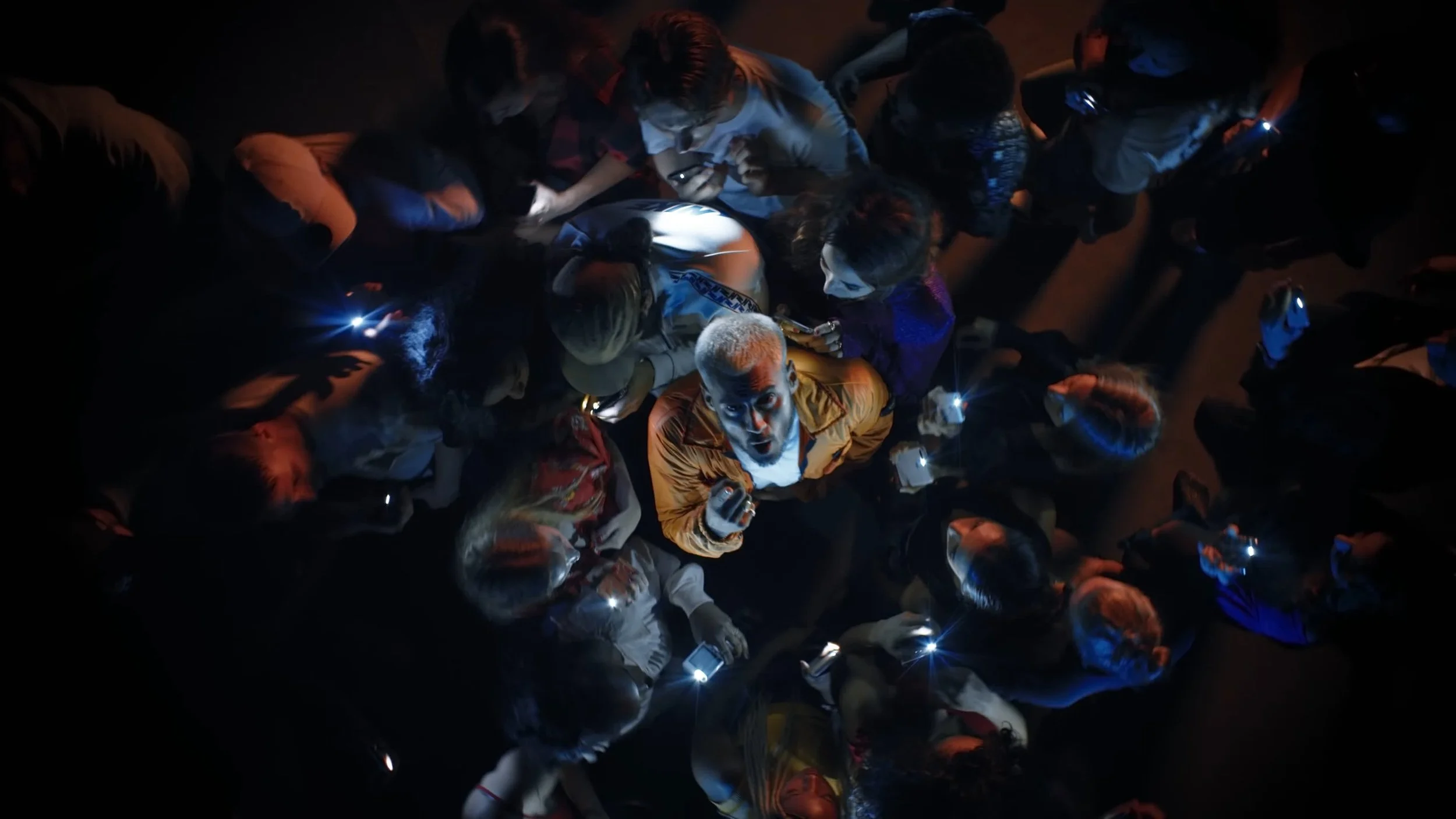 Crowd of people surrounding a person looking up with flashlights in a dark environment.
