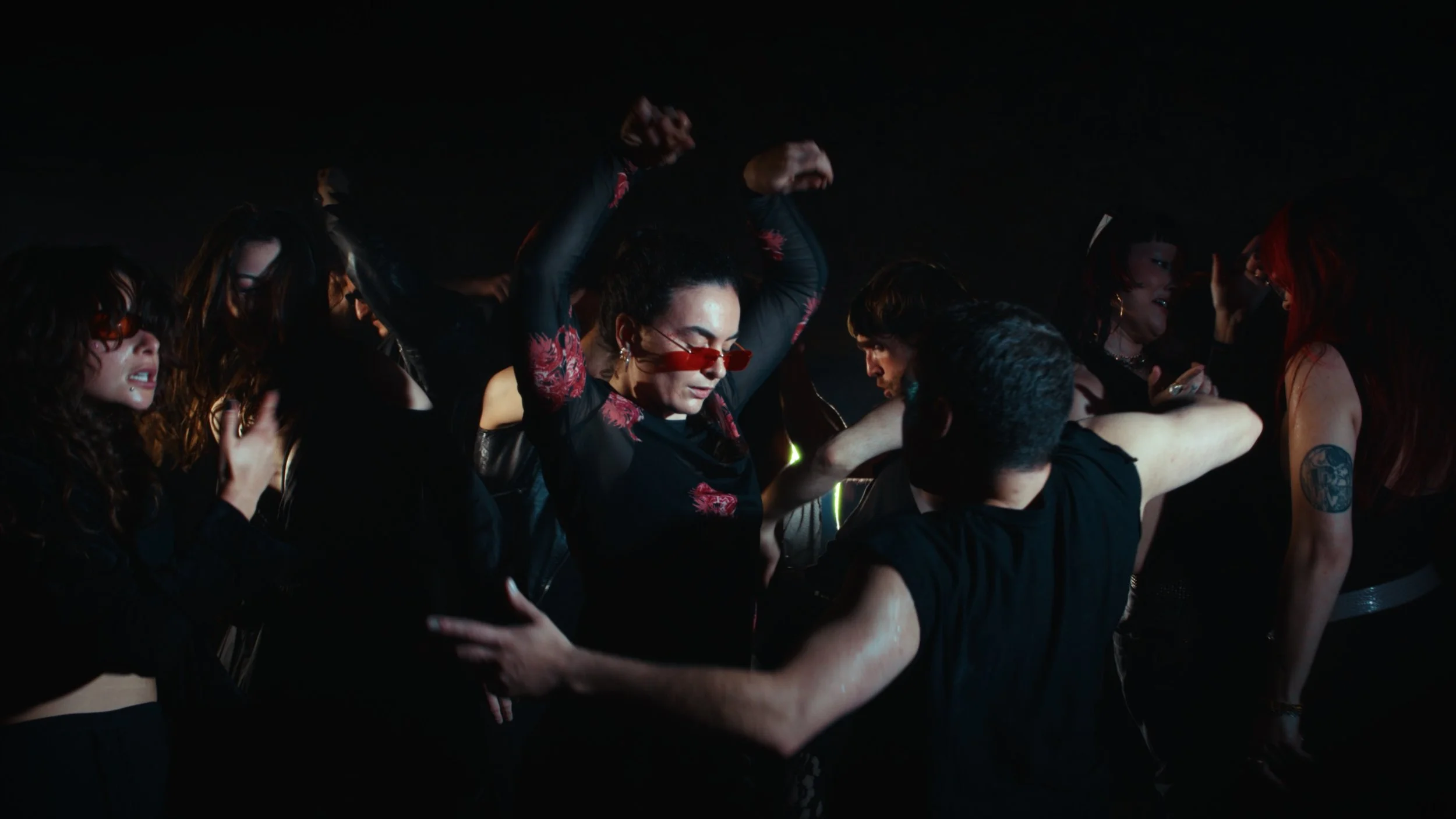 Group of women dancing and socializing at a dark, lively party or nightclub, with some wearing sunglasses and dressed in black.