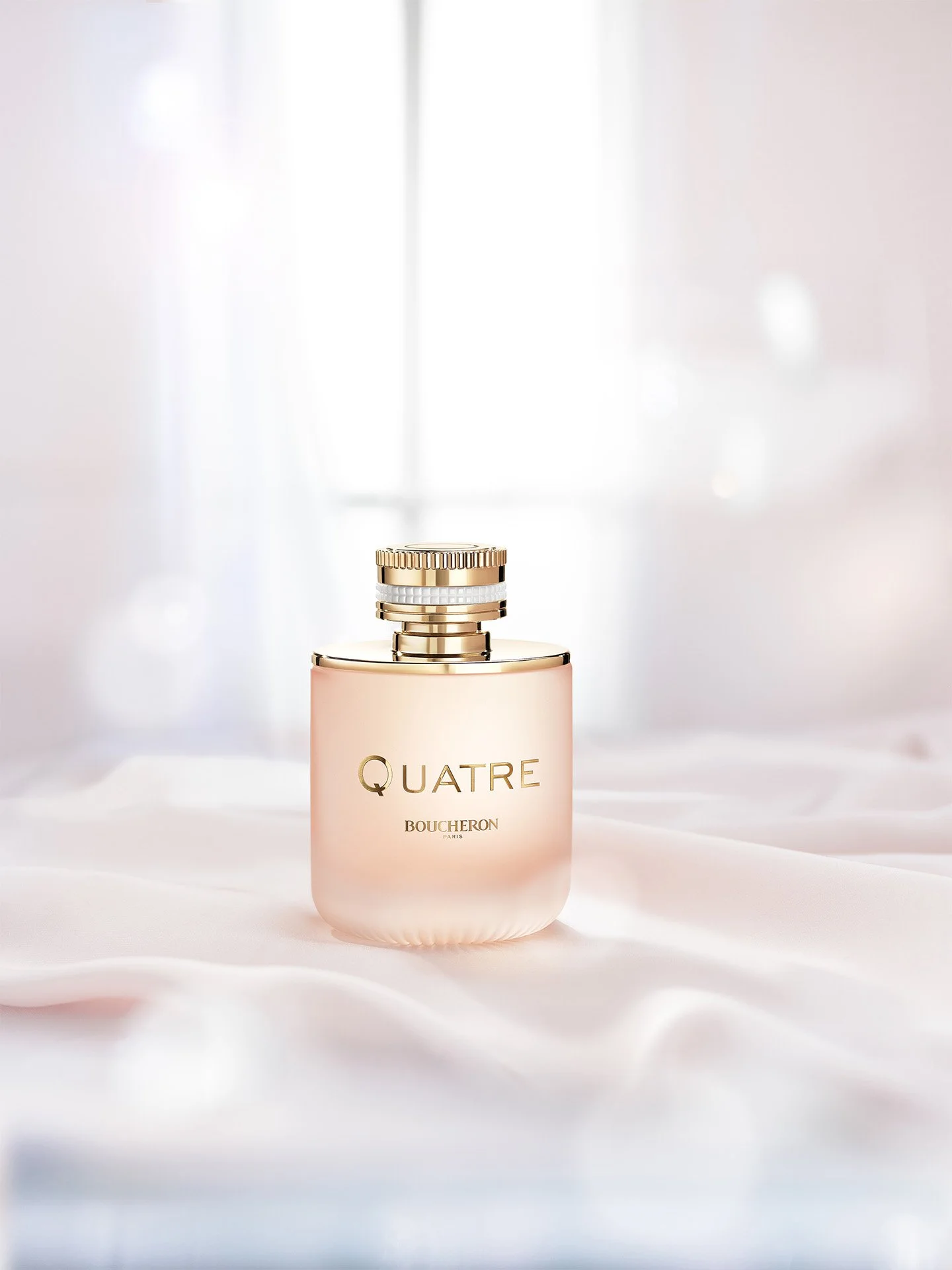 A perfume bottle labeled "Quatre by Boucheron" on a soft, white fabric background in a well-lit setting.