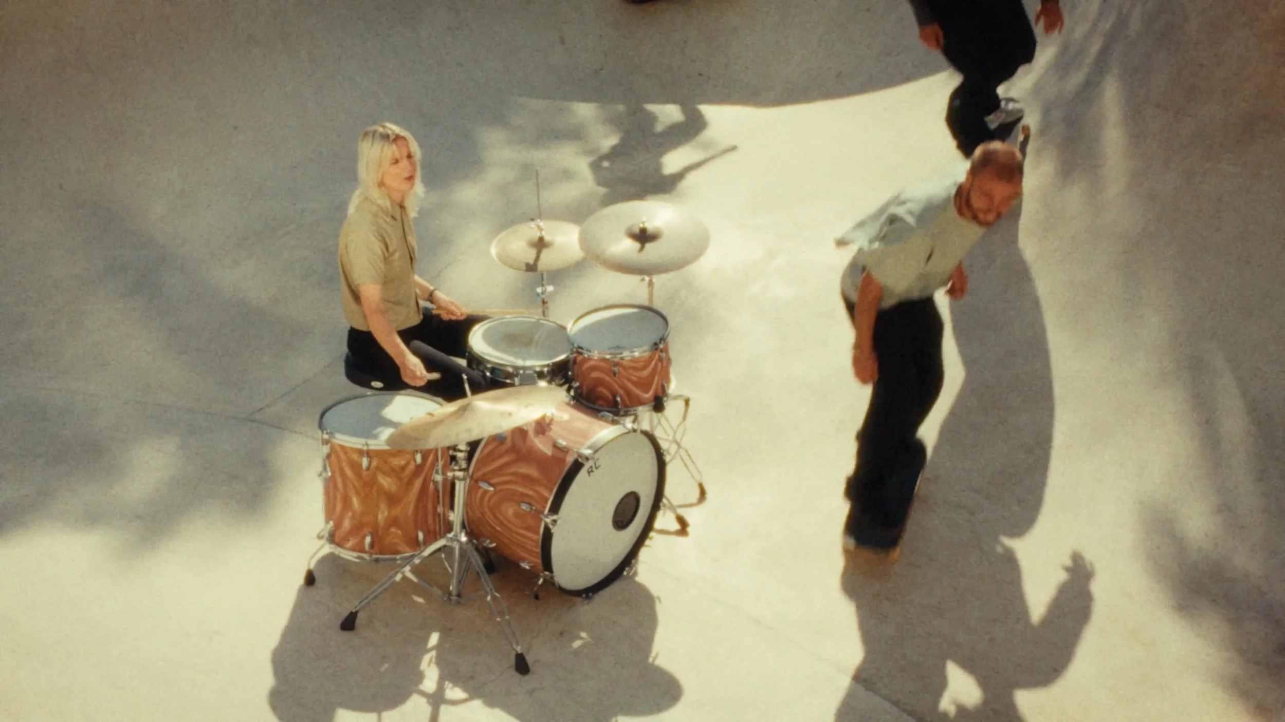 Marion Brunetto from the band Requin Chagrin sitting at a drum set with a drummer's drumming stance, appearing to be performing, with shadows of skateboarders in the background.