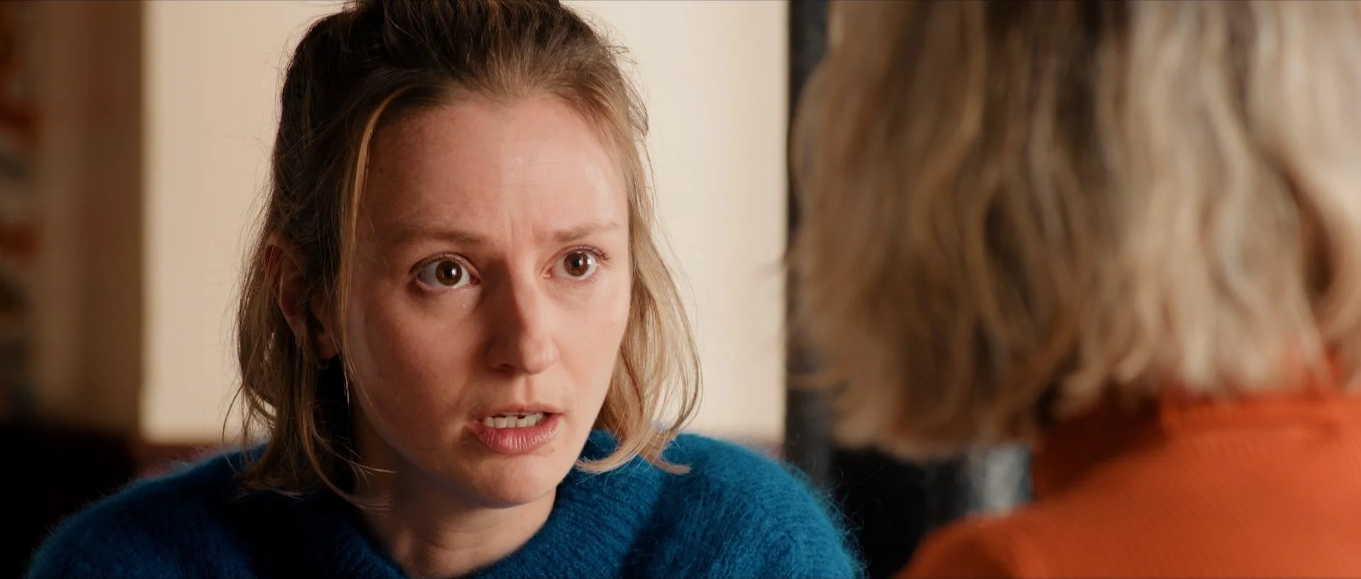 Tiphaine Daviot with shoulder-length light brown hair, wearing a blue sweater, appears to be speaking to someone off-camera, with a serious or intense expression.