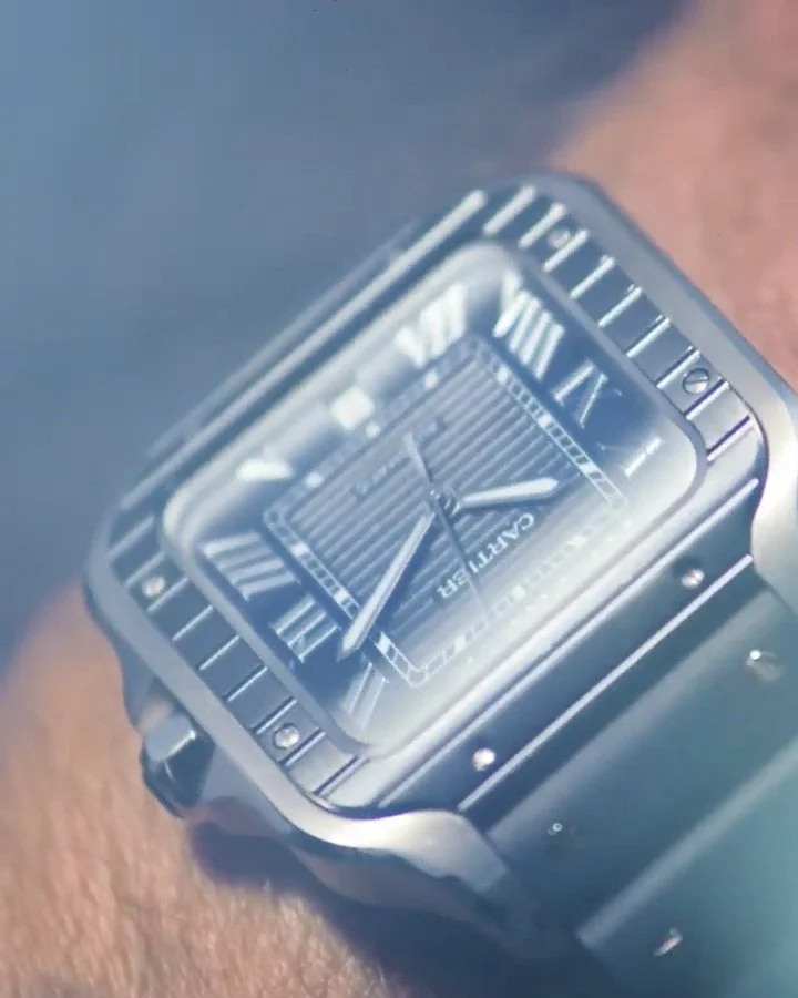 Close-up of a luxury Cartier Santos wristwatch with a rectangular face and Roman numerals.