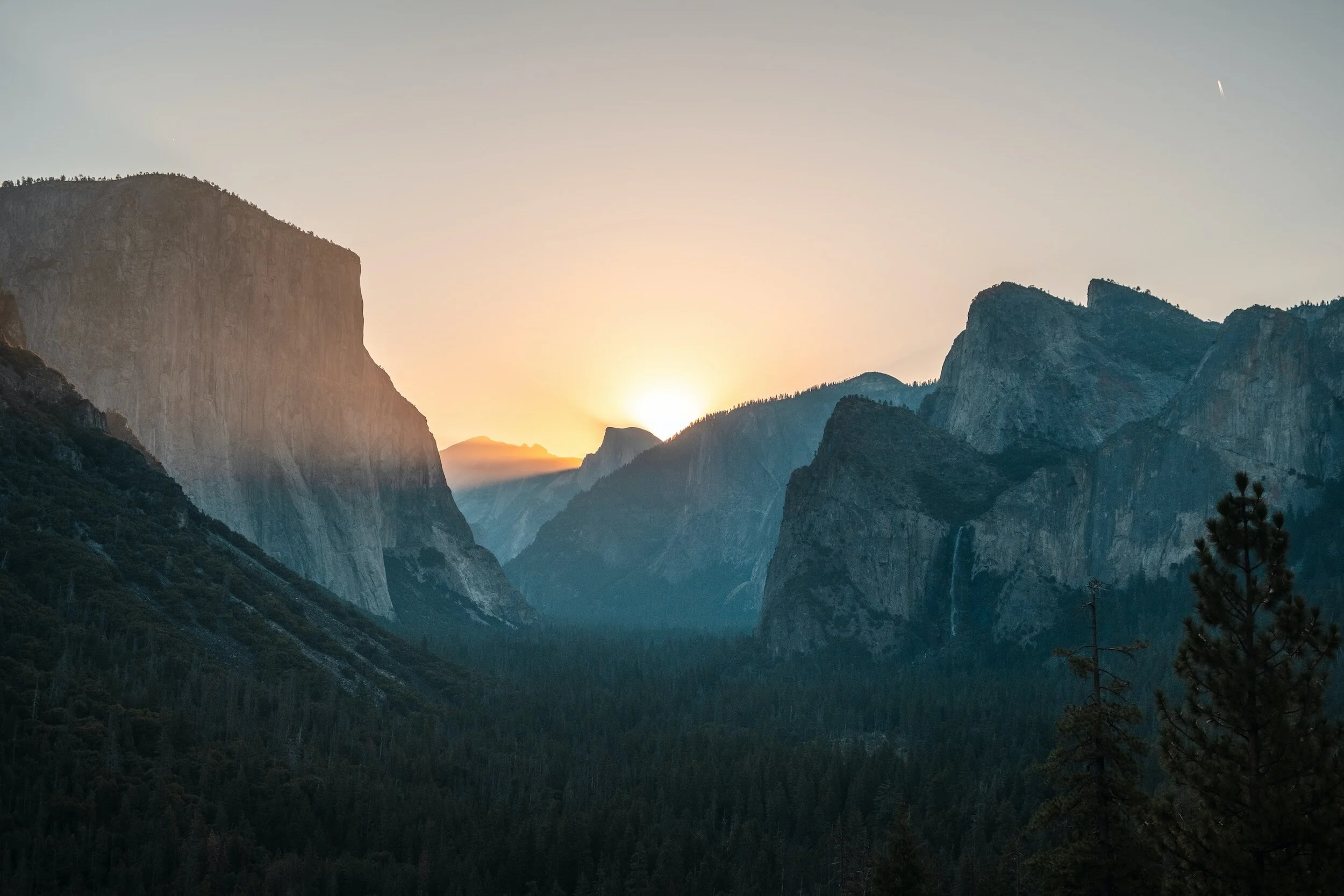 Sunrise over mountains in Yosemite National Park, showcasing El Capitan and Half Dome with a valley in the foreground.