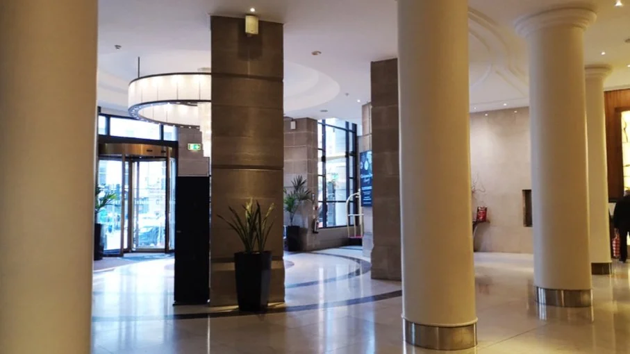 Hotel lobby with tall cream-colored columns, large windows, and indoor plants.