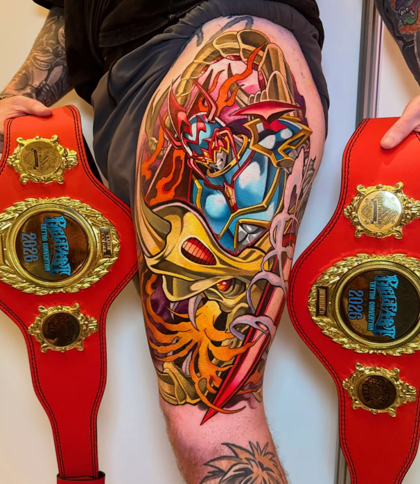 Colorful tattoo of a fierce tiger with red eyes, a blue robotic creature with red accents, and fiery flames, displayed on a person's thigh, flanked by two championship belts with gold embellishments and blue center plates.