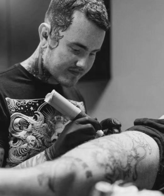 Tattoo artist inking a detailed tattoo on a client's arm in black and white.