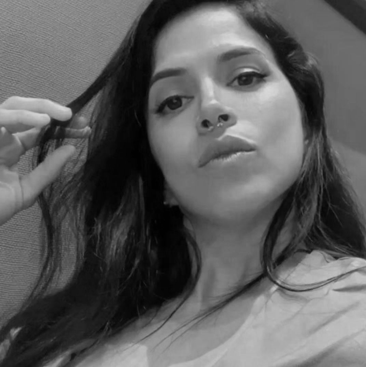 Black and white close-up photo of a woman with long hair, holding a strand of her hair with her left hand, looking at the camera with a neutral expression.