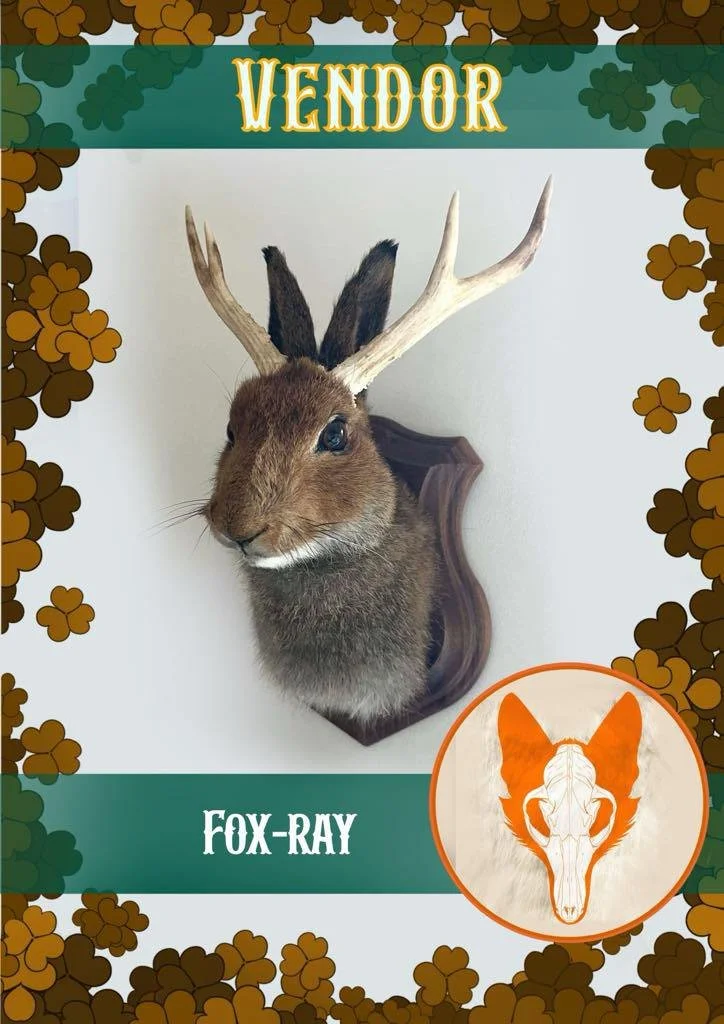 Mounted animal head with fox's face and antlers, labeled as "Fox-Ray" on a framed display with leaf and clover decorative border.