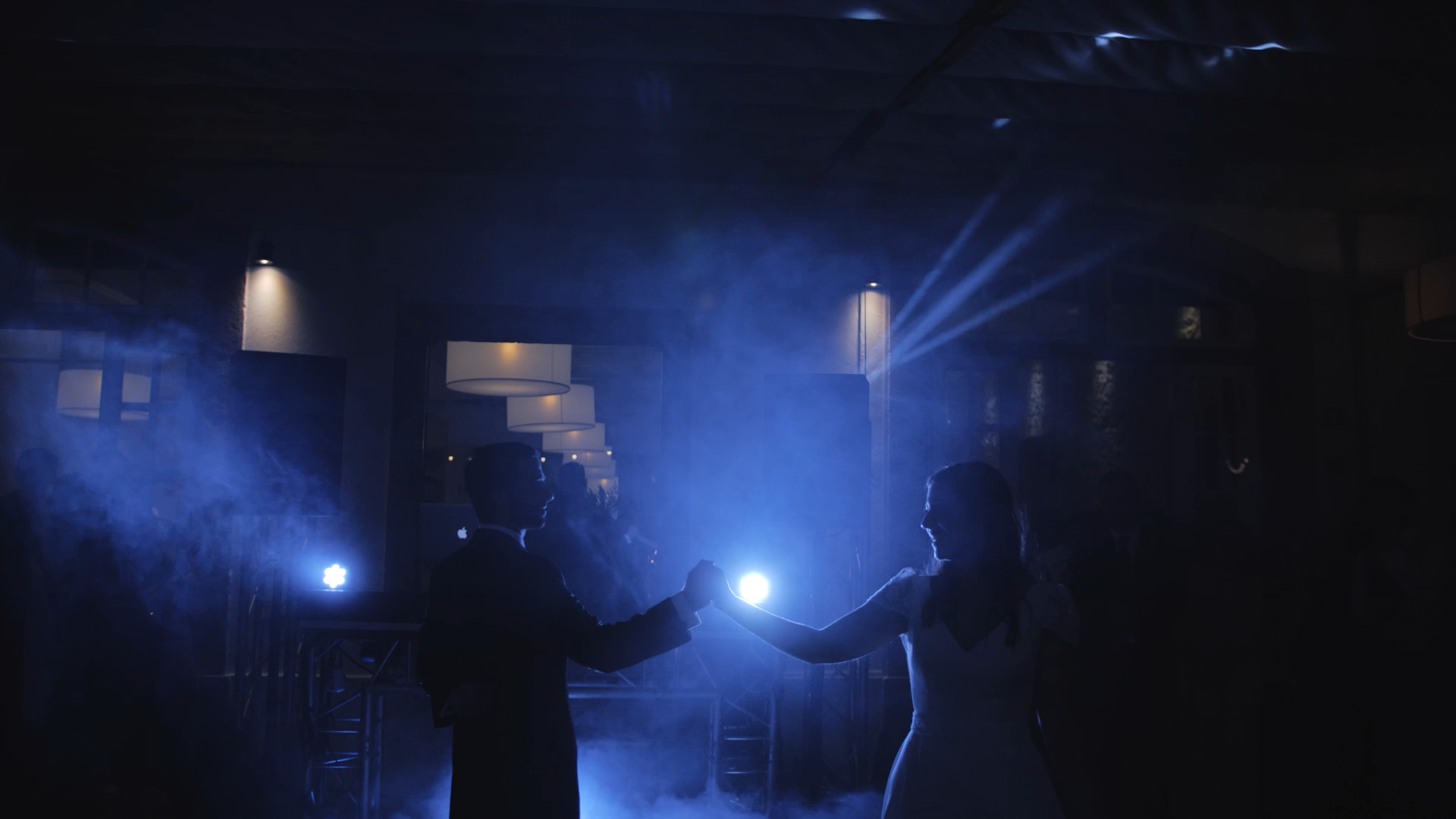 Casal dançando sob luzes azuis em um ambiente escuro, possivelmente durante uma festa ou casamento.