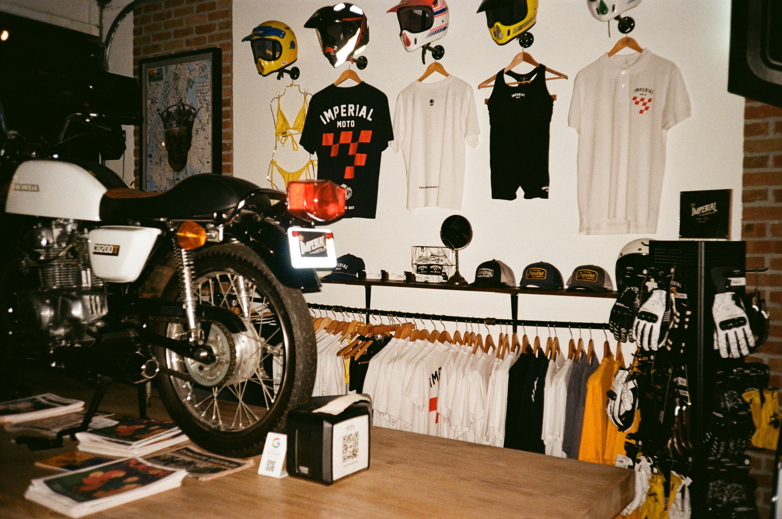Display of motorcycle apparel and accessories, including helmets, t-shirts, hats, gloves, and jackets in a retail store.