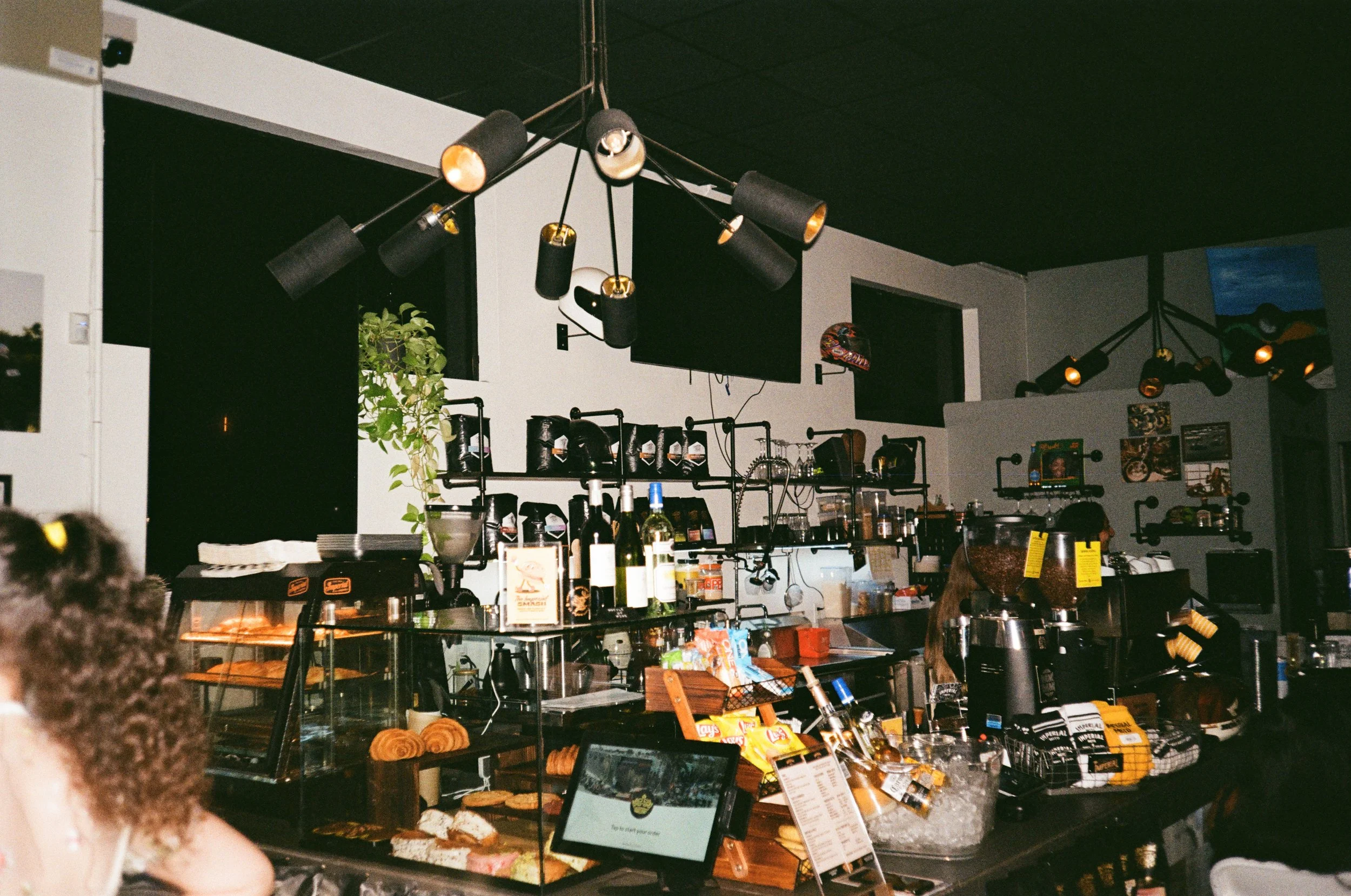 Interior of a cafe or coffee shop with food display, barista equipment, and modern lighting fixtures.