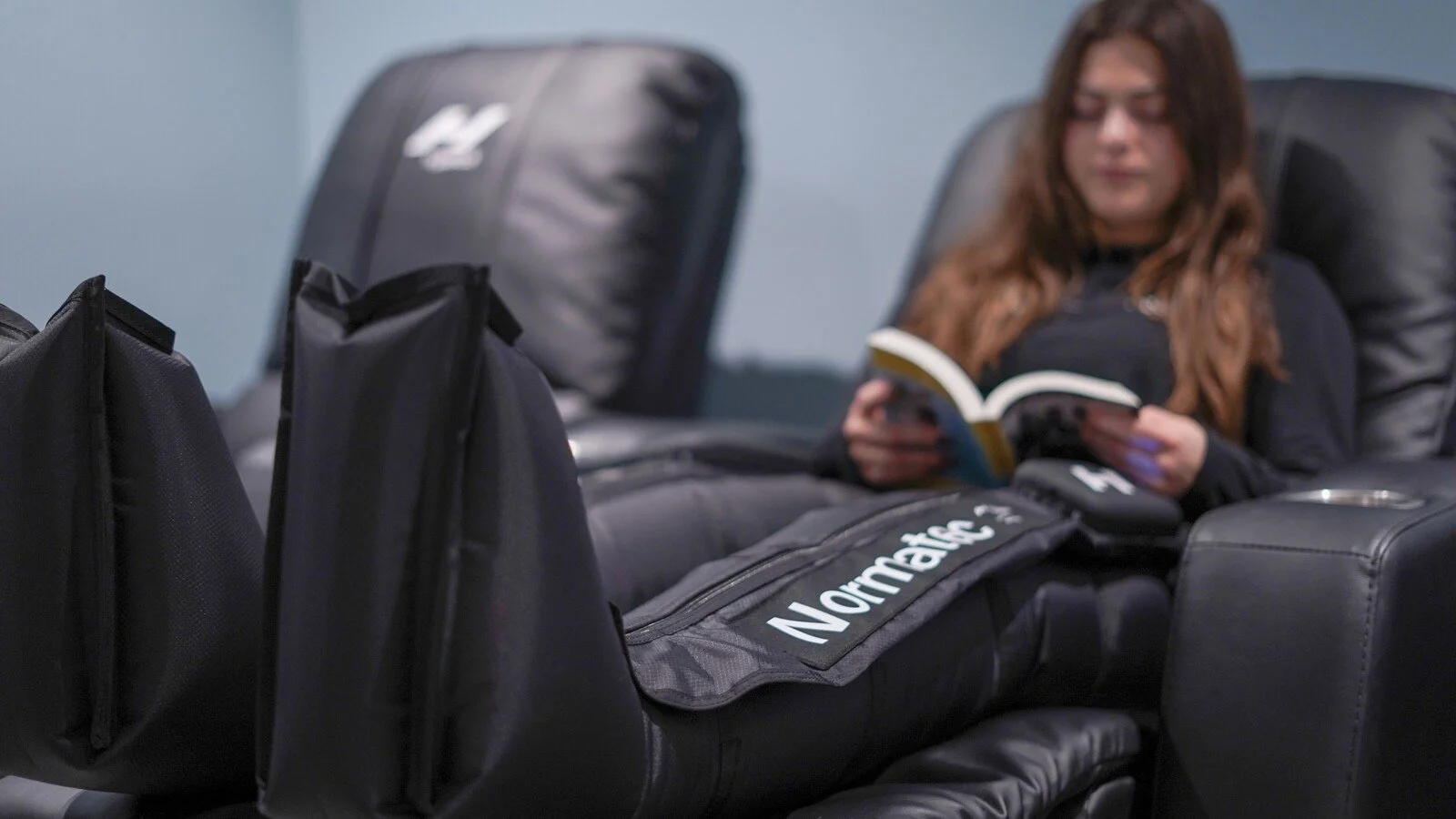 Massage room with three black recliners and hanging massage boots on the wall.