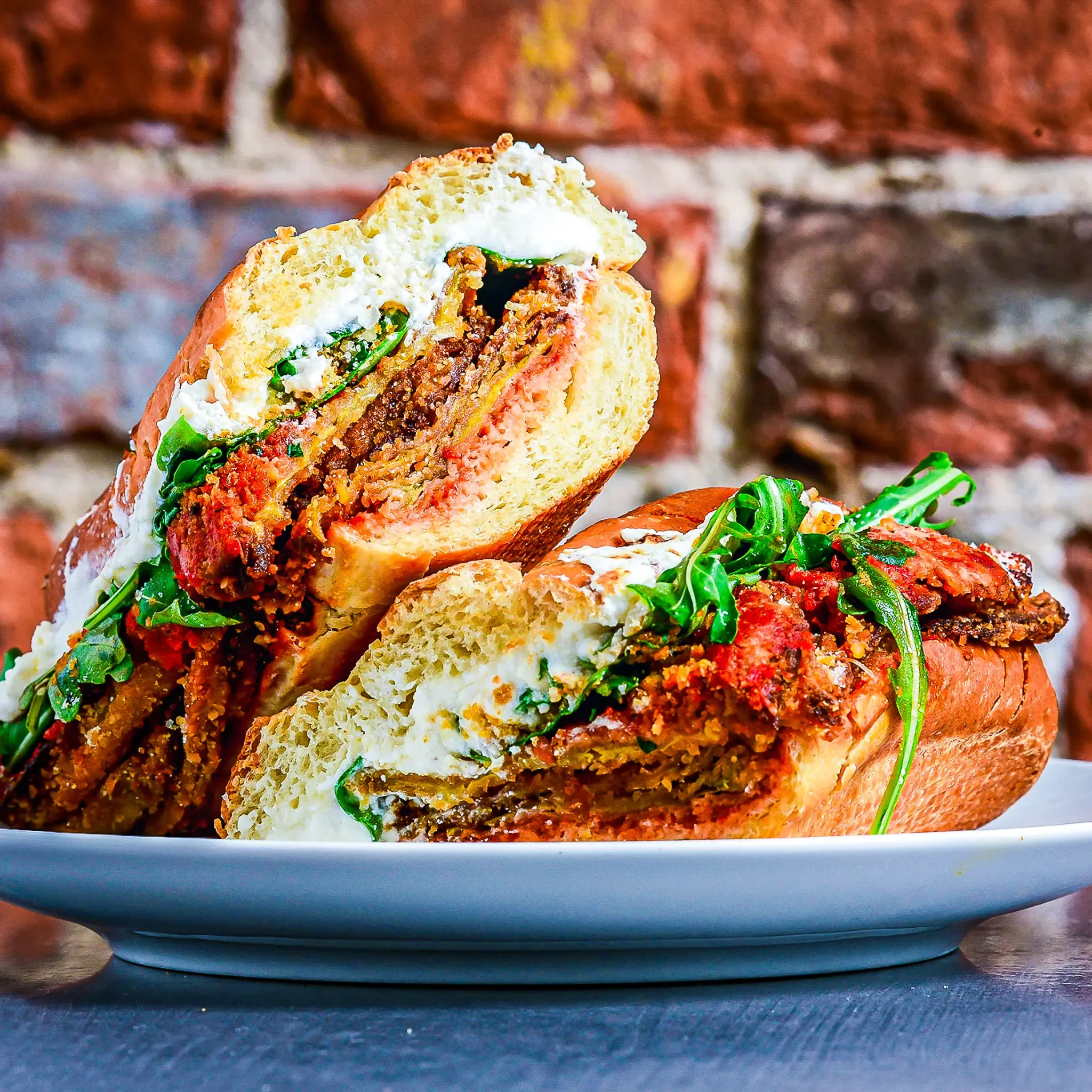Sandwell's Spicy Eggplant Parm vegetarian sub — baked eggplant cutlet with whipped burrata, marinara, parmesan, Calabrian chile oil, toasted breadcrumbs, and arugula on a house-baked semolina roll, available at Sandwell sandwich shops in NYC