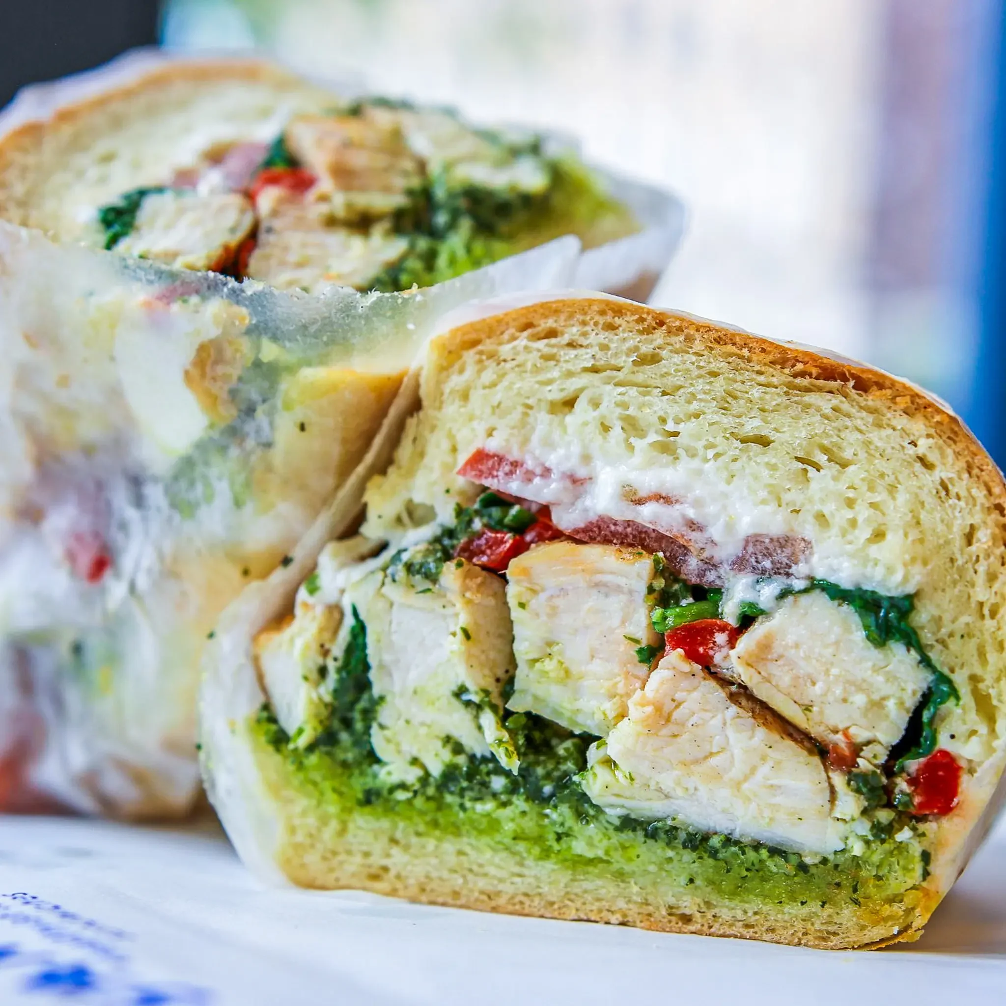 Sandwell's Chicken Pesto Burrata sandwich — grilled chicken breast with basil pesto, whipped burrata, roasted red peppers, tomato, and spinach on a house-baked semolina roll, available at Sandwell sandwich shops in NYC