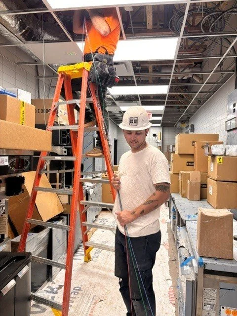 An electrician on a ladder and another electrician holding wire