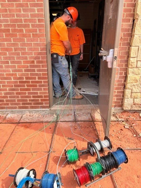 Two electricians pulling wire through a doorway. Spools of wire are on the ground. 