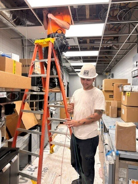 An electrician on a ladder and another electrician holding wire