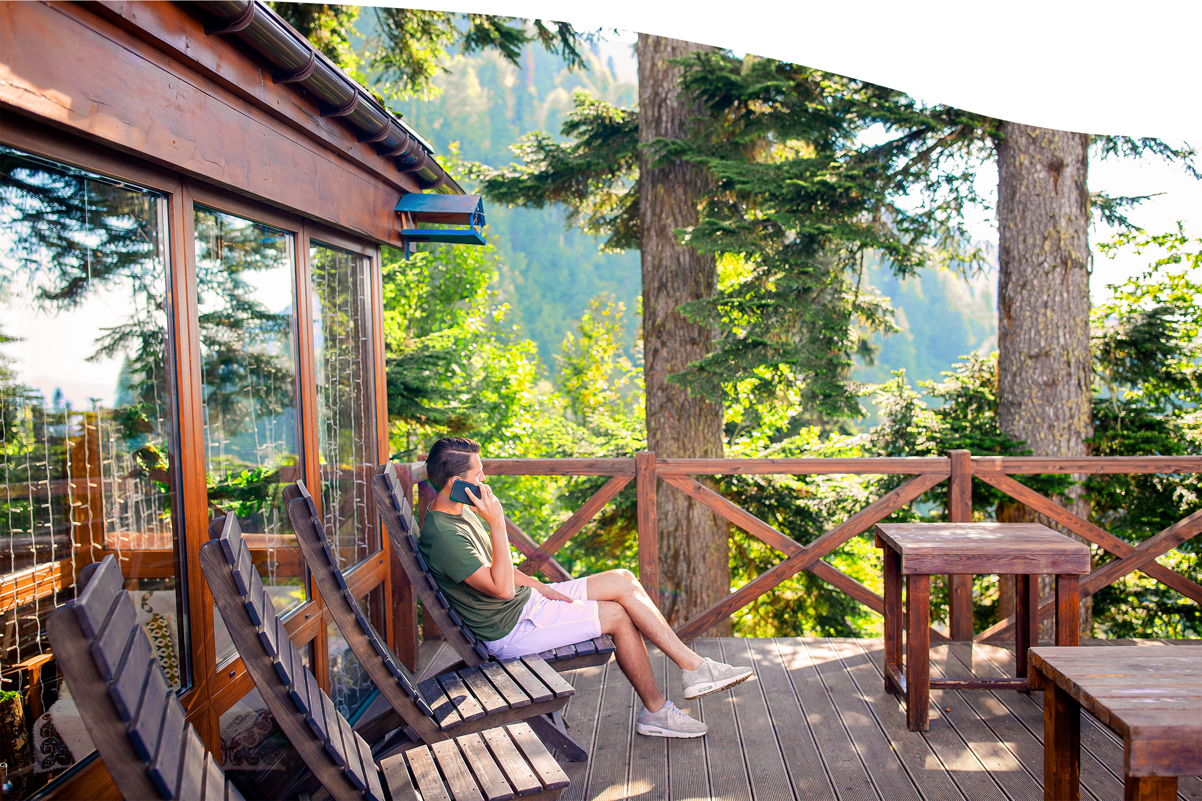 Man on a cabin deck in the mountains talking on his phone