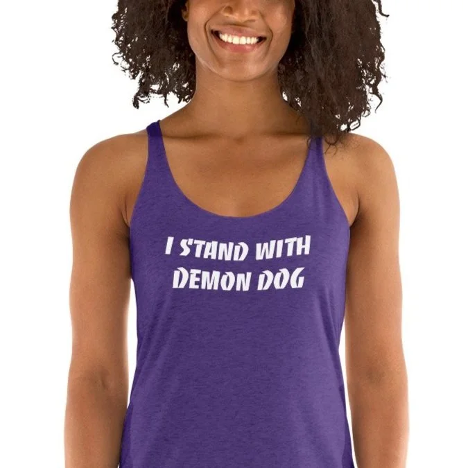 A woman wearing a purple tank top that reads 'I STAND WITH DEMON DOG' in white text.