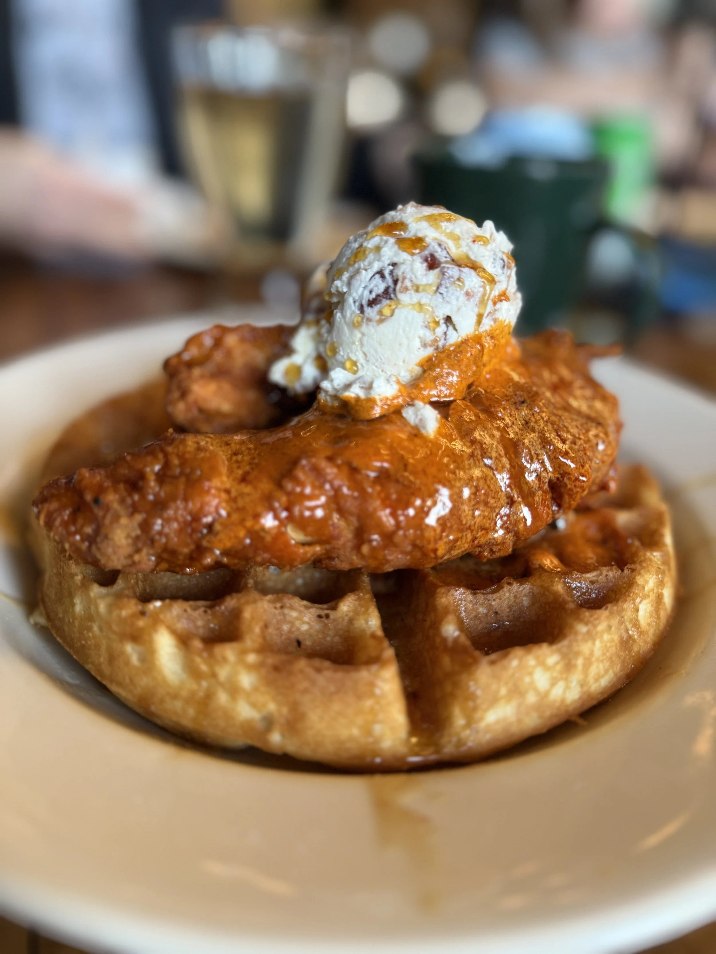 A plate with a waffle topped with fried chicken, a dollop of whipped cream, and caramel syrup.