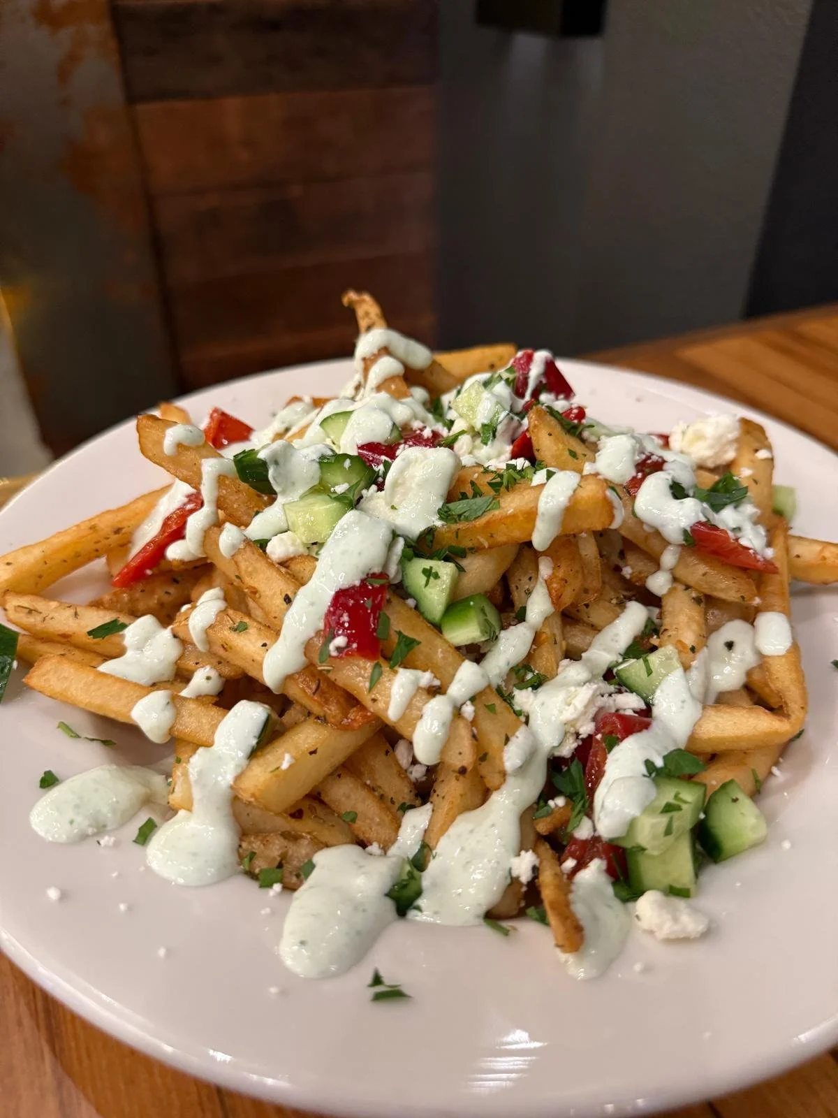 Plate of seasoned French fries topped with chopped cucumbers, tomatoes, parsley, and drizzled with white sauce.