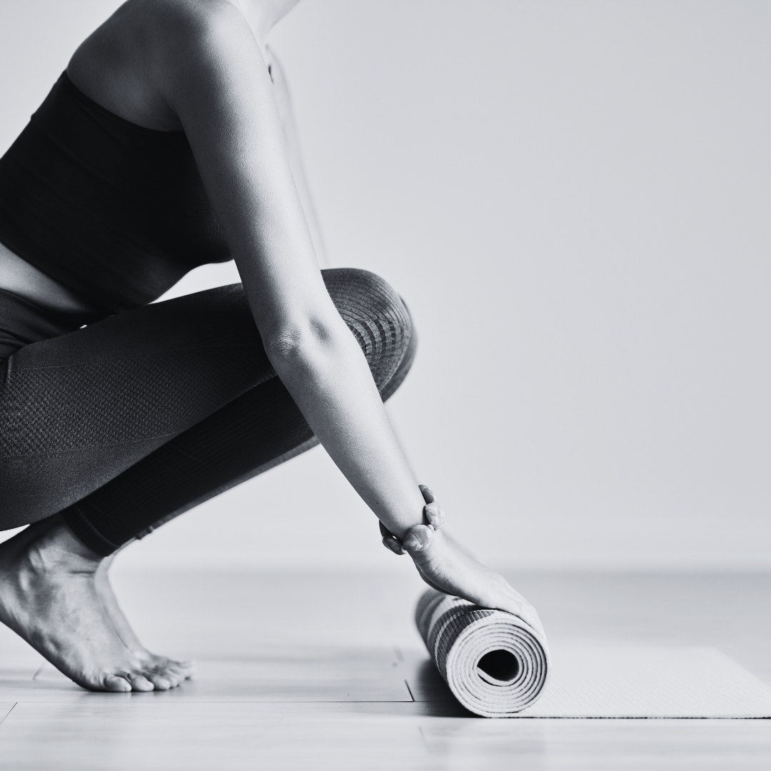 A person in athletic clothing adjusting a yoga mat on the floor.