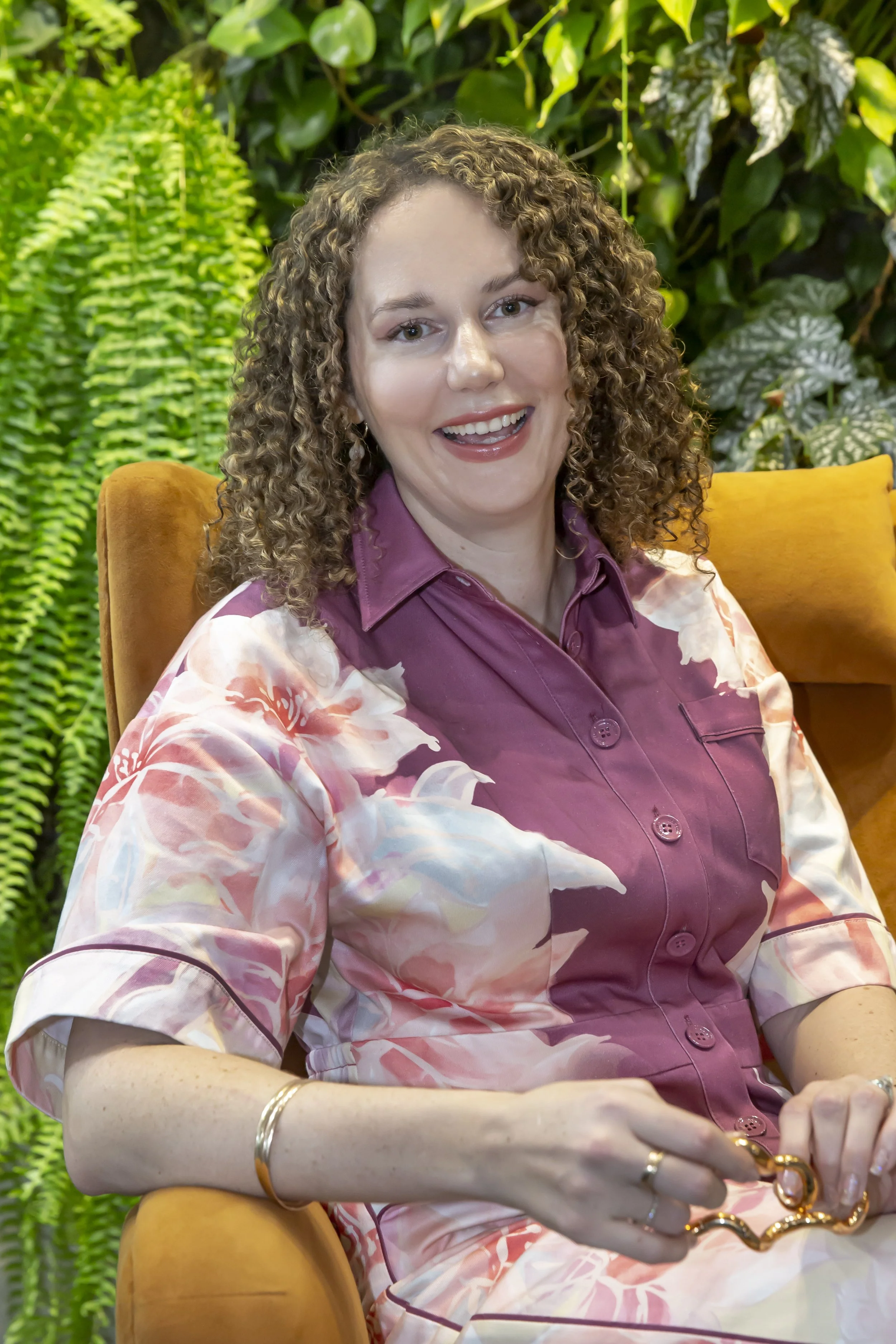 Monique sits on an orange couch and smiling directly at the camera.