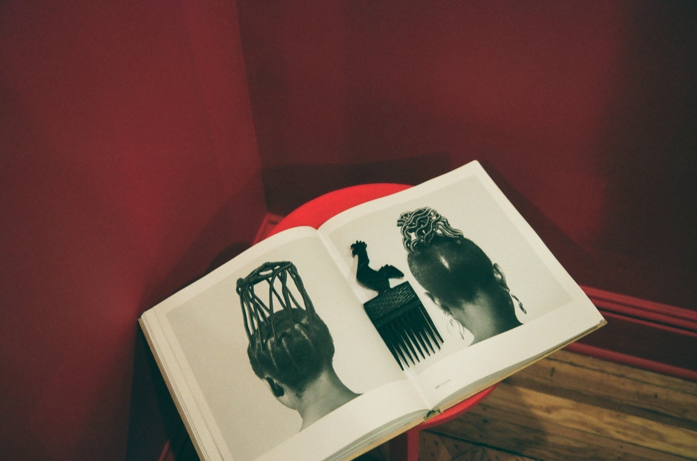 Open book with black and white collage of African hairstyle images, placed on a red circular table against a dark red wall.