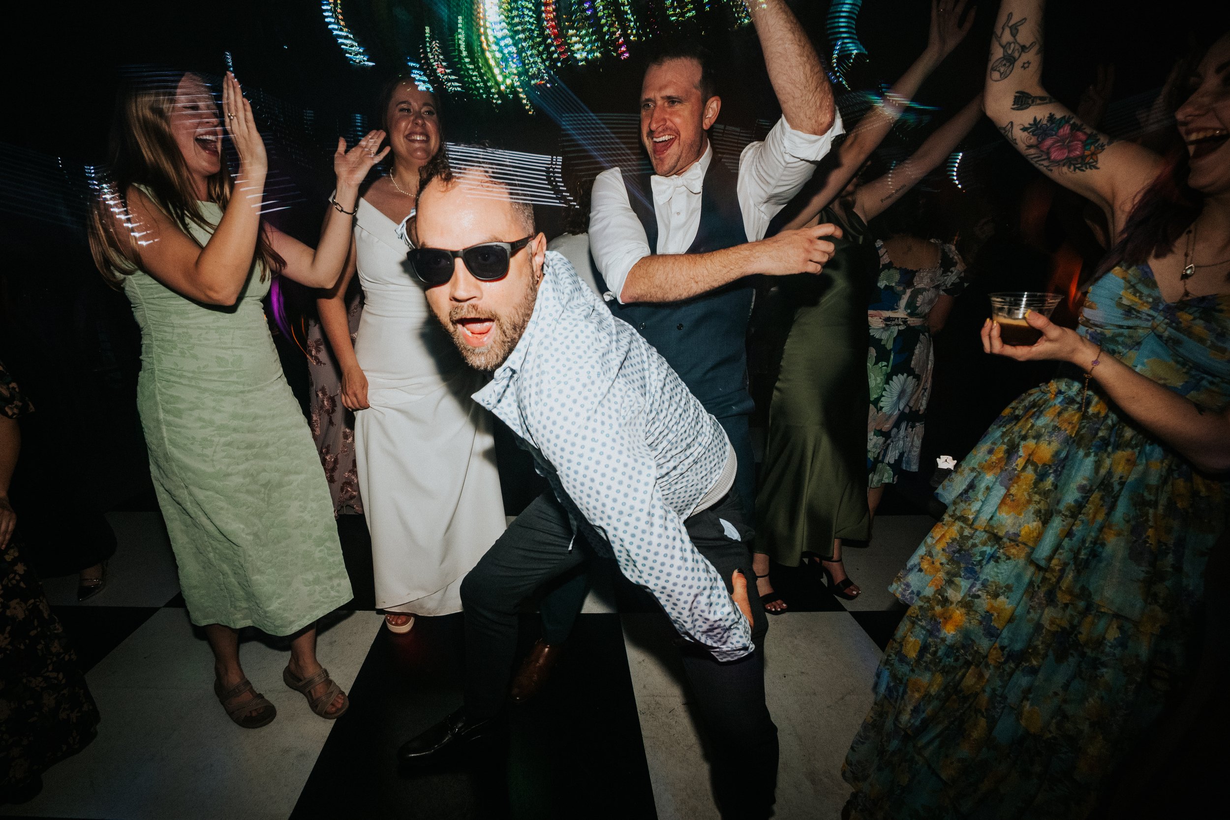 A group of people dancing and celebrating at a party or nightclub, with colorful lights and a festive atmosphere.