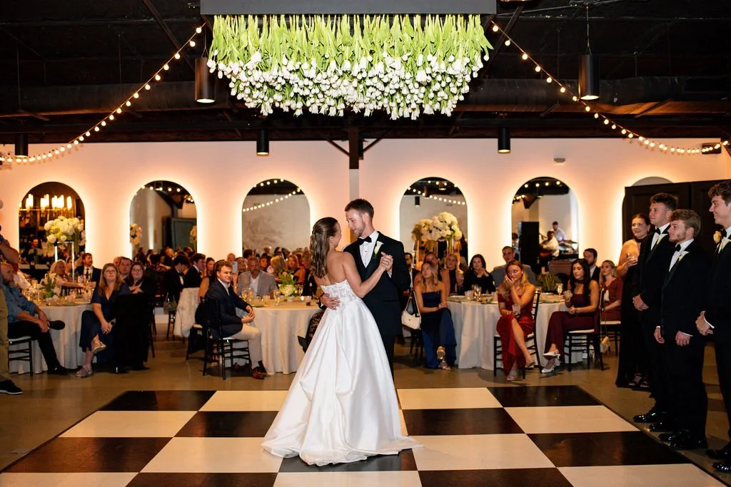 Bride and groom dancing at their wedding reception with guests seated at tables in the background.
