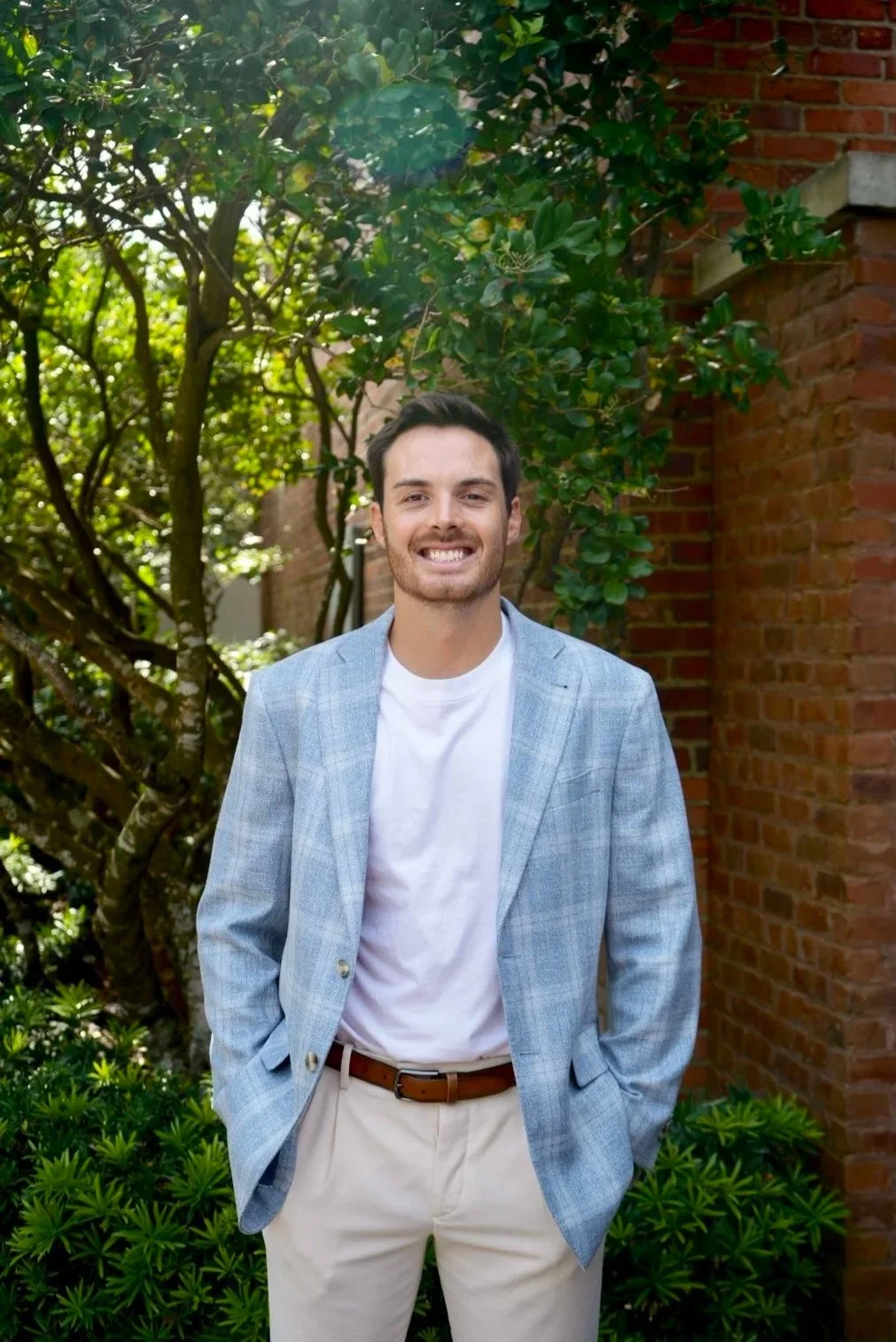 Clancy the bar and event manager is a young man with dark hair and a bright smile, wearing a black shirt, standing in a restaurant with warm lighting and a chandelier overhead.