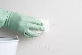 Person wearing green gloves cleaning a white wall with a cloth.