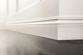 Close-up of a white baseboard along a wall and hardwood flooring.