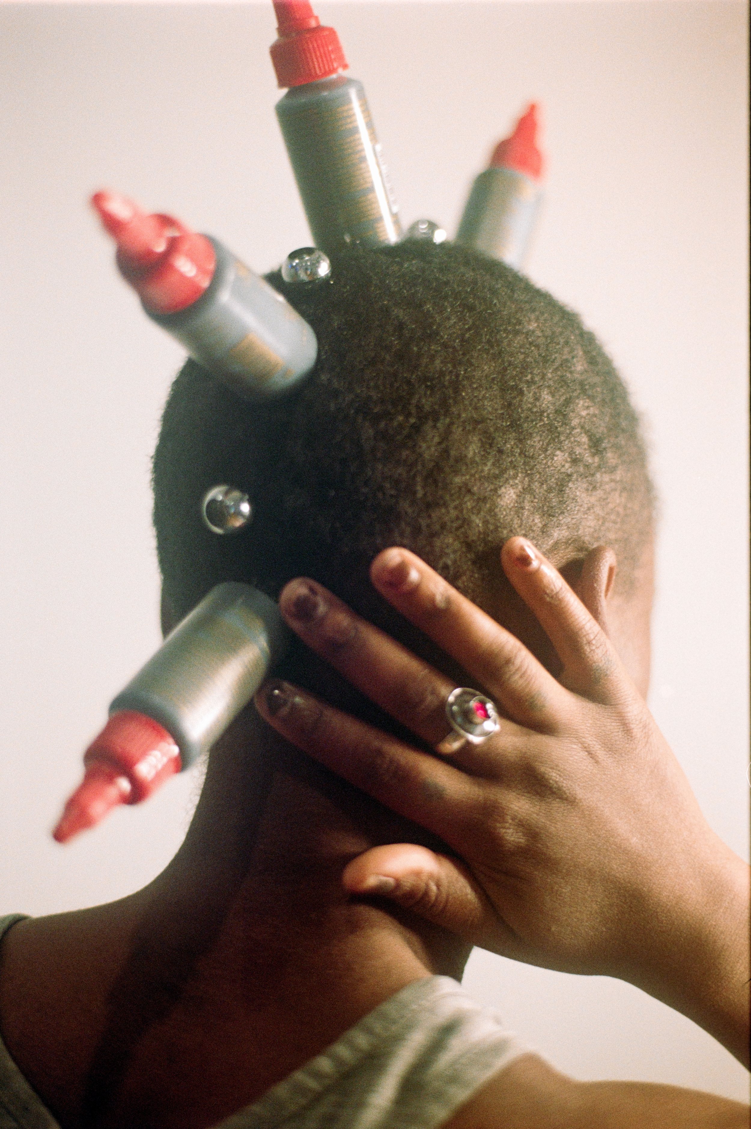 A person with dark skin holding a dark textured ball with multiple silver and red markers embedded in it. Several smaller silver markers are also attached to the ball. The person is wearing a ring on one finger and a gray and white striped sleeve.