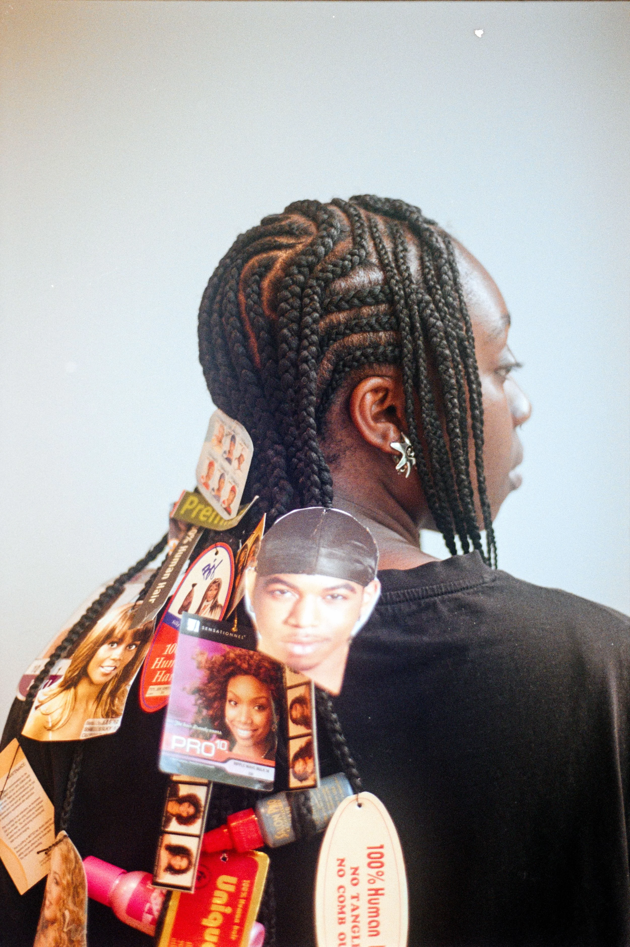 Close-up of a woman's head showcasing her long, intricate, braided hairstyle with beads and tags hanging from the braids, surrounded by magazines or brochures.