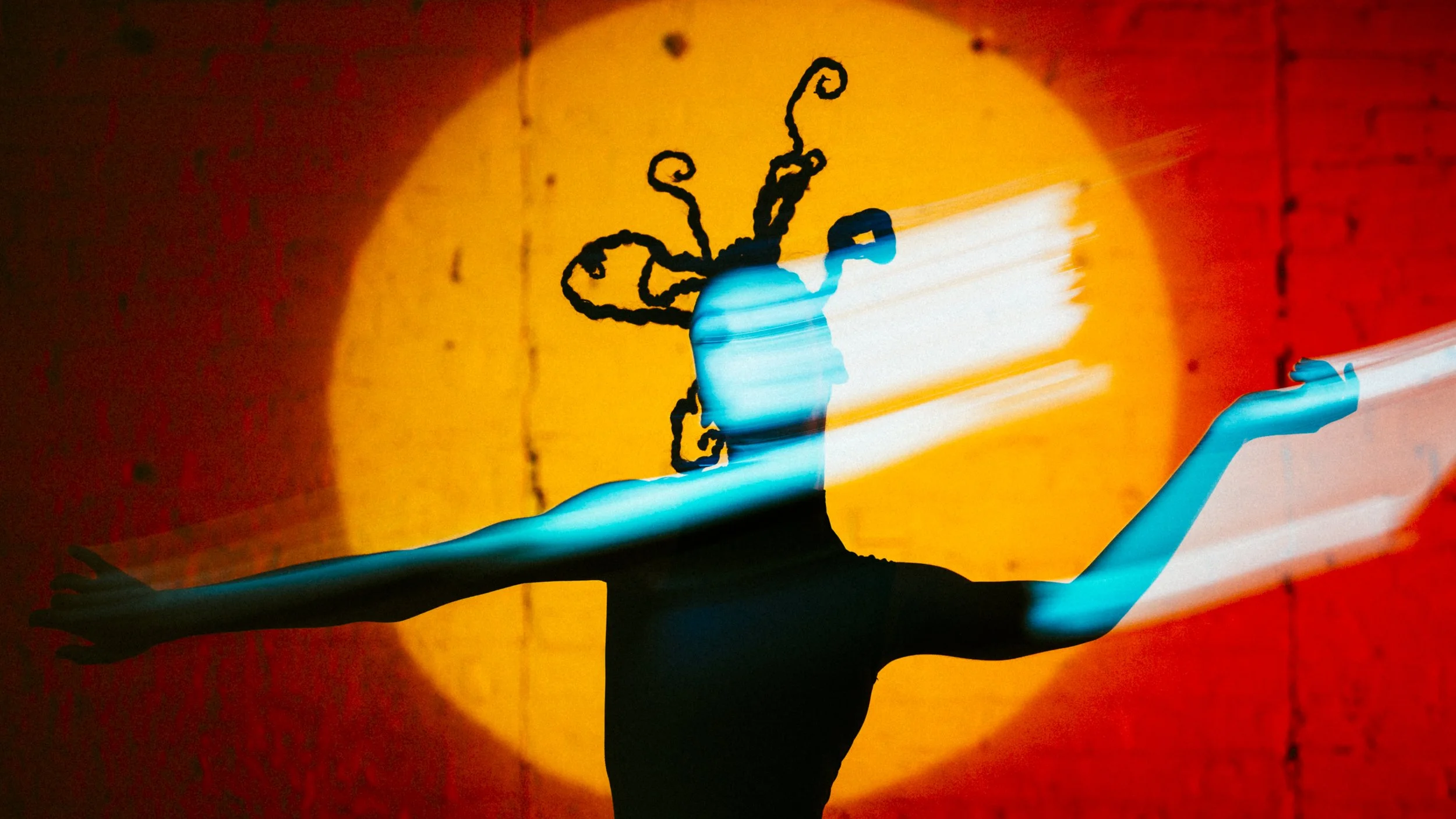 A silhouette of a person with outstretched arms, holding a light source that creates a colorful glow with an abstract, whimsical drawing of a creature with antennas and curled appendages on the wall behind.