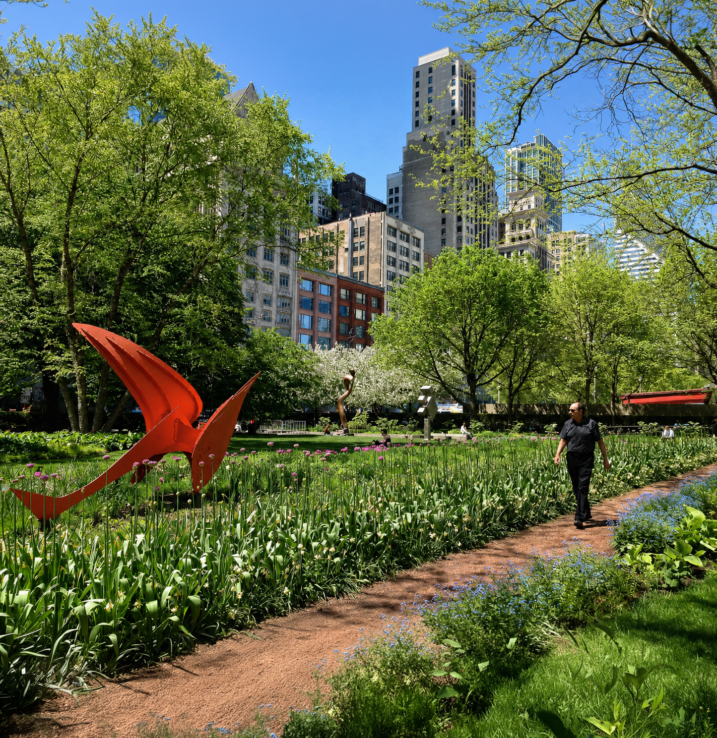 Downtown park filled with spring greenery and flowers, red abstract sculptures, a walking path, and high-rise buildings in the background.