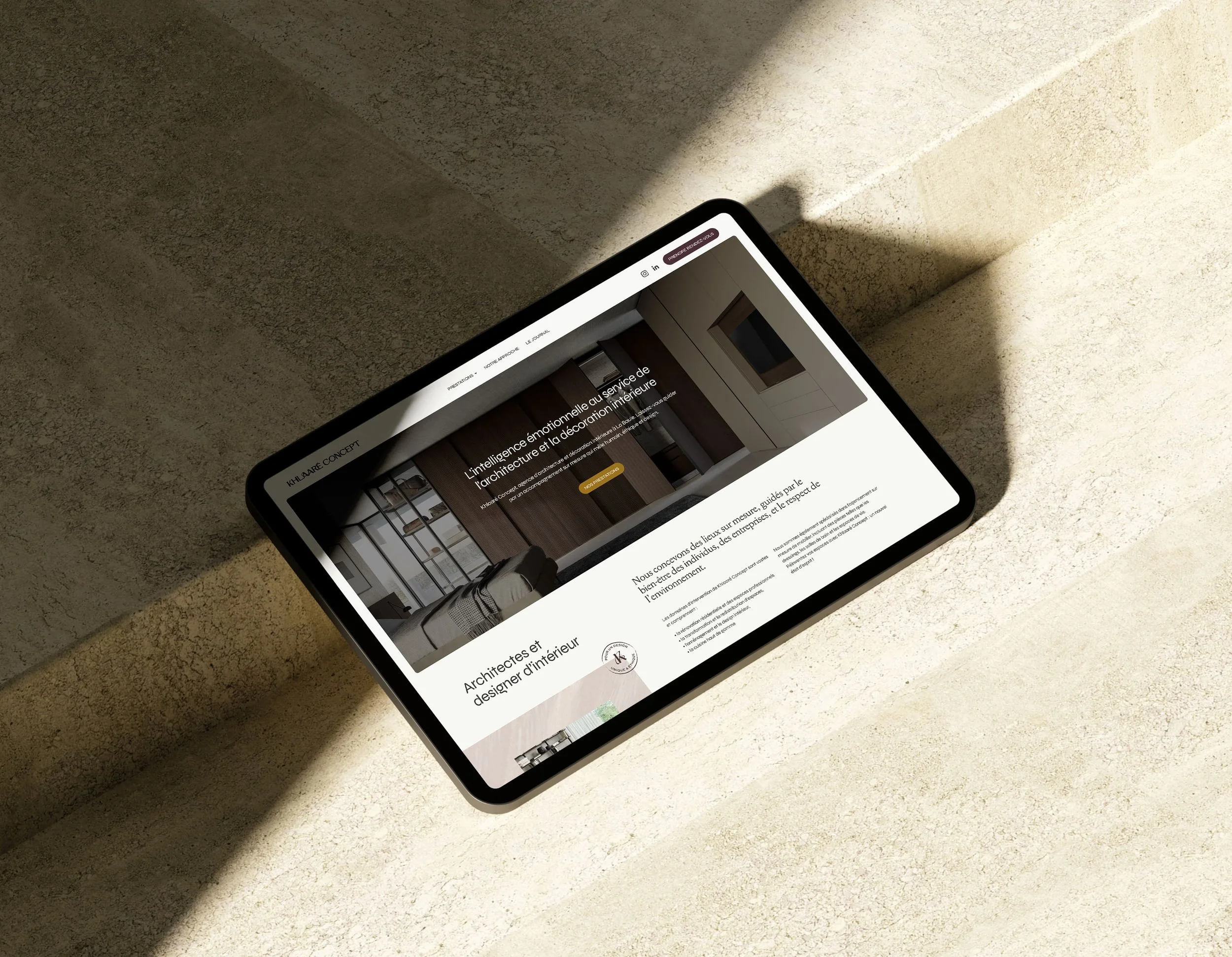 Une tablette posée sur une surface en pierre avec l'écran affichant une page web d'une agence d'architecture et de décoration intérieure, ambiance moderne et minimaliste.