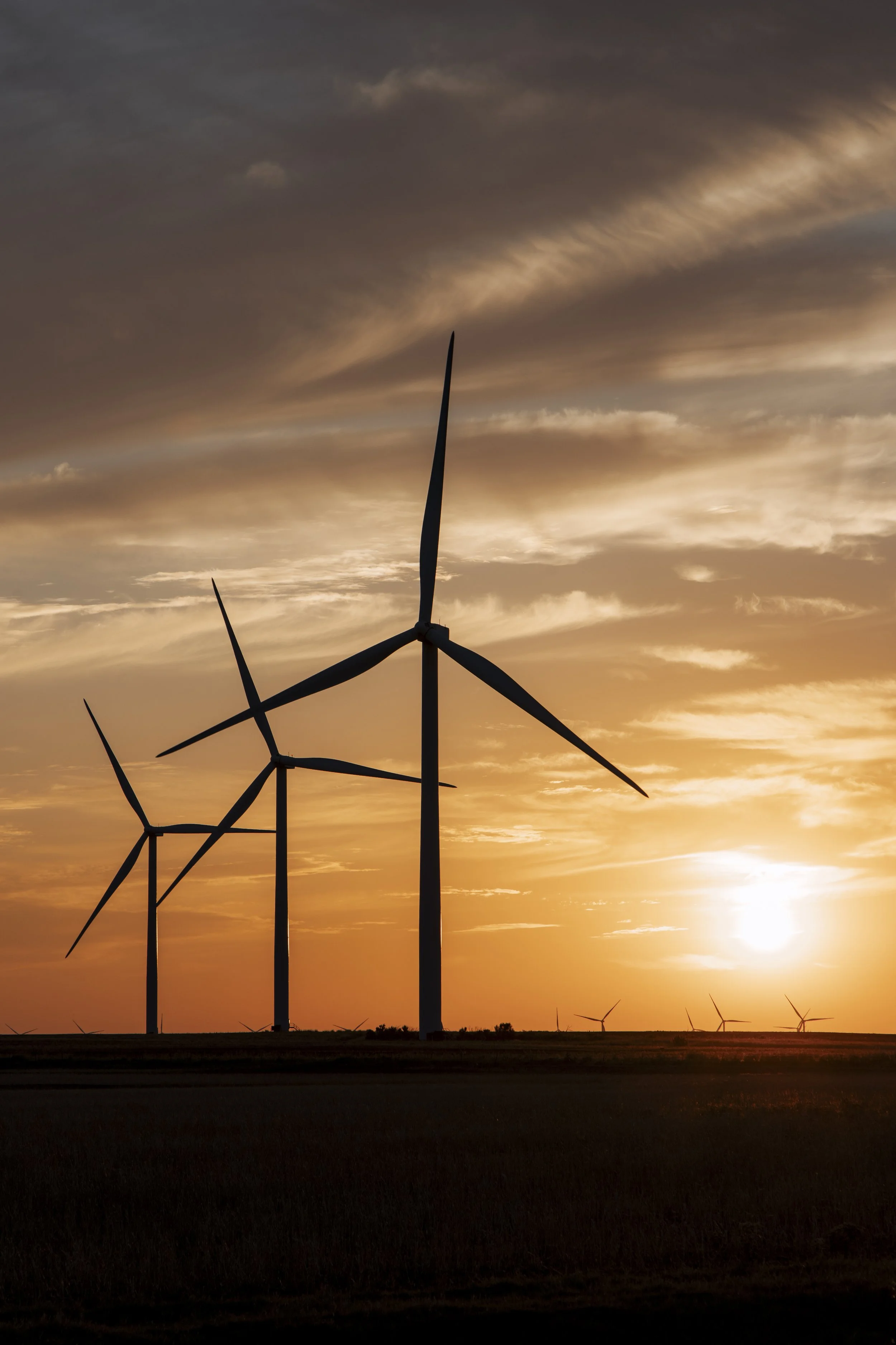 Wind turbines silhouetted against a sunset sky with orange and purple clouds.