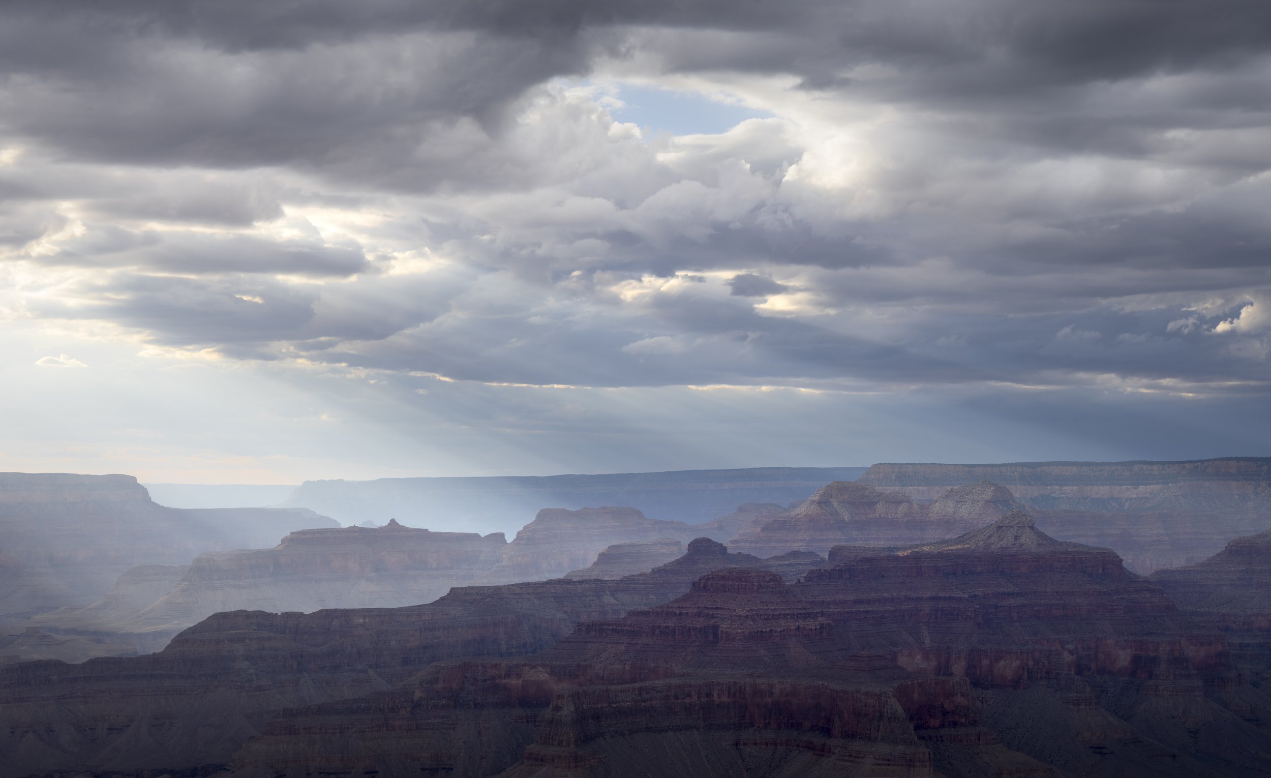 View of the Grand Canyon under a cloudy sky, showing layered rock formations and ridges.