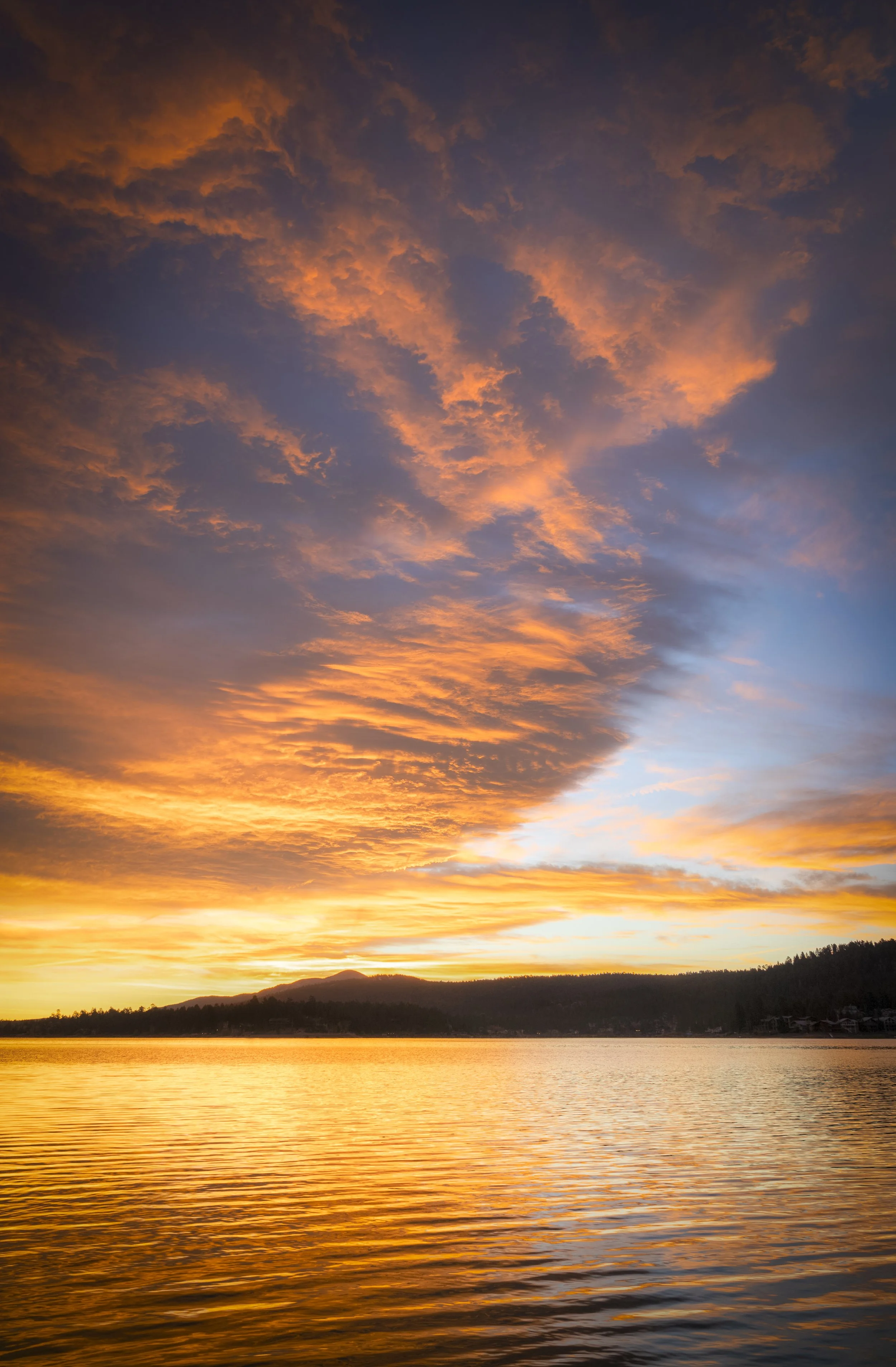 A vibrant sunset over a body of water with colorful clouds and distant hills.