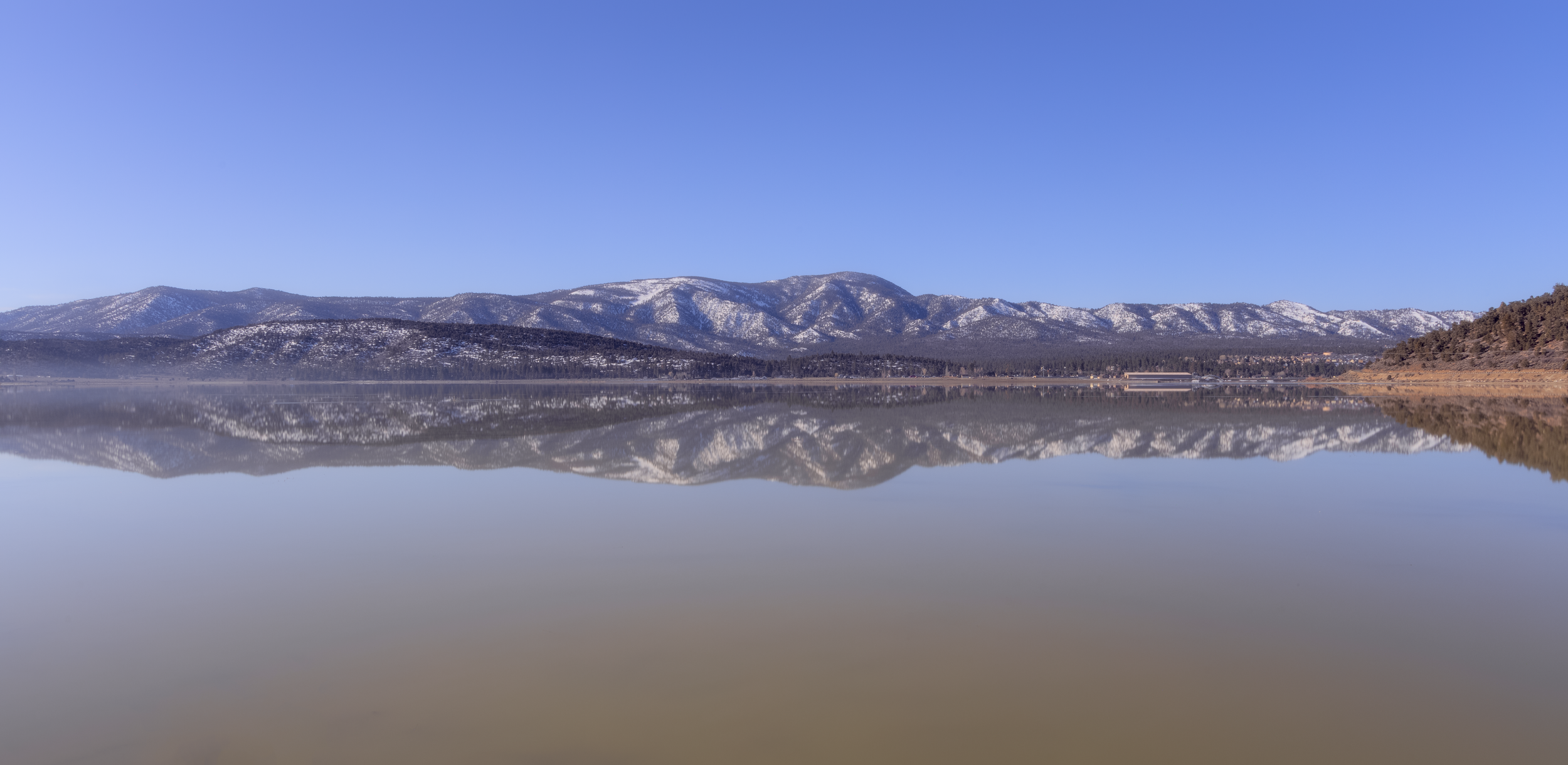 Calm lake with snow-capped mountains and clear blue sky reflected in the water.