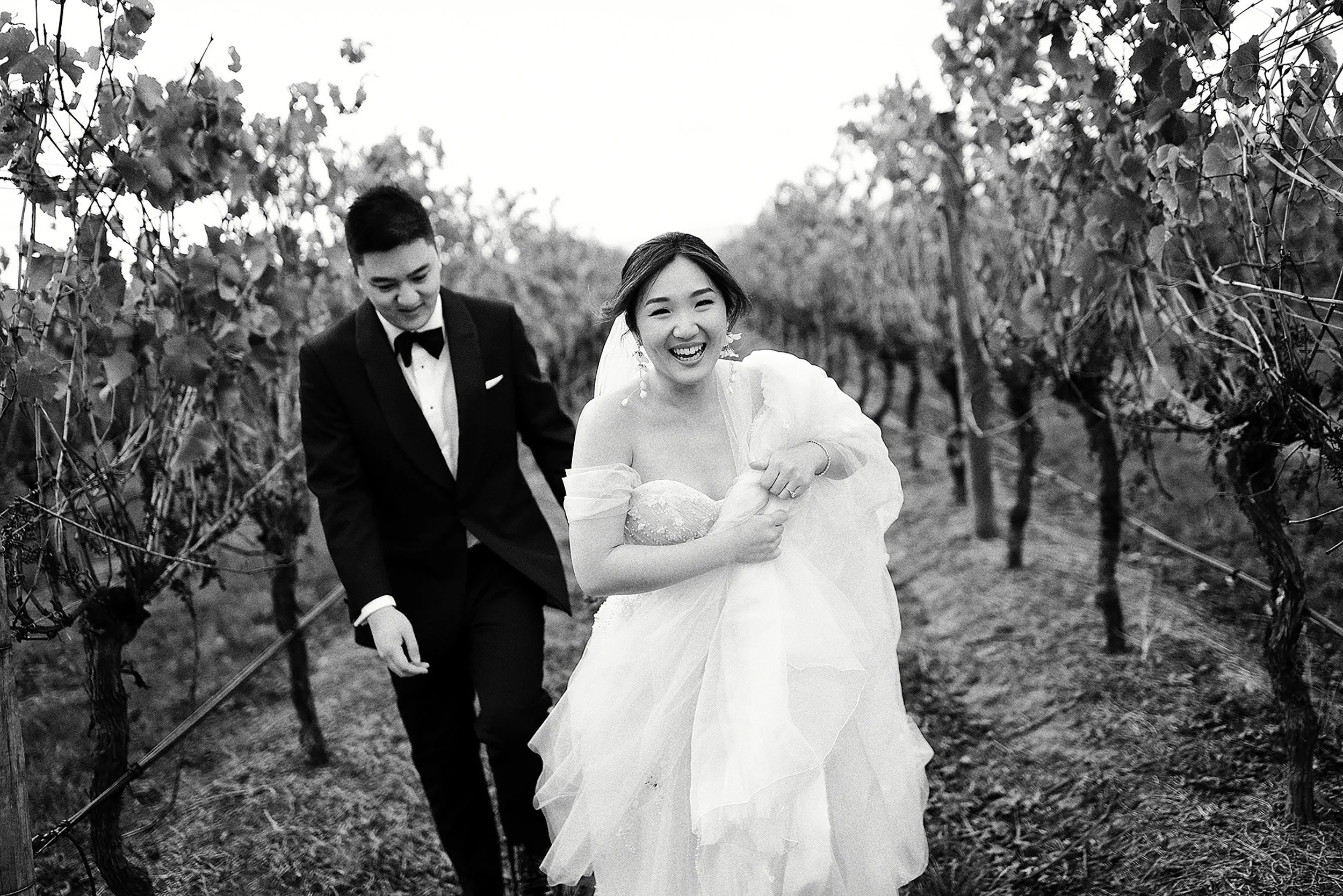 Bride and groom walking through vineyard rows at Stones of the Yarra Valley, candid black and white documentary wedding photo.