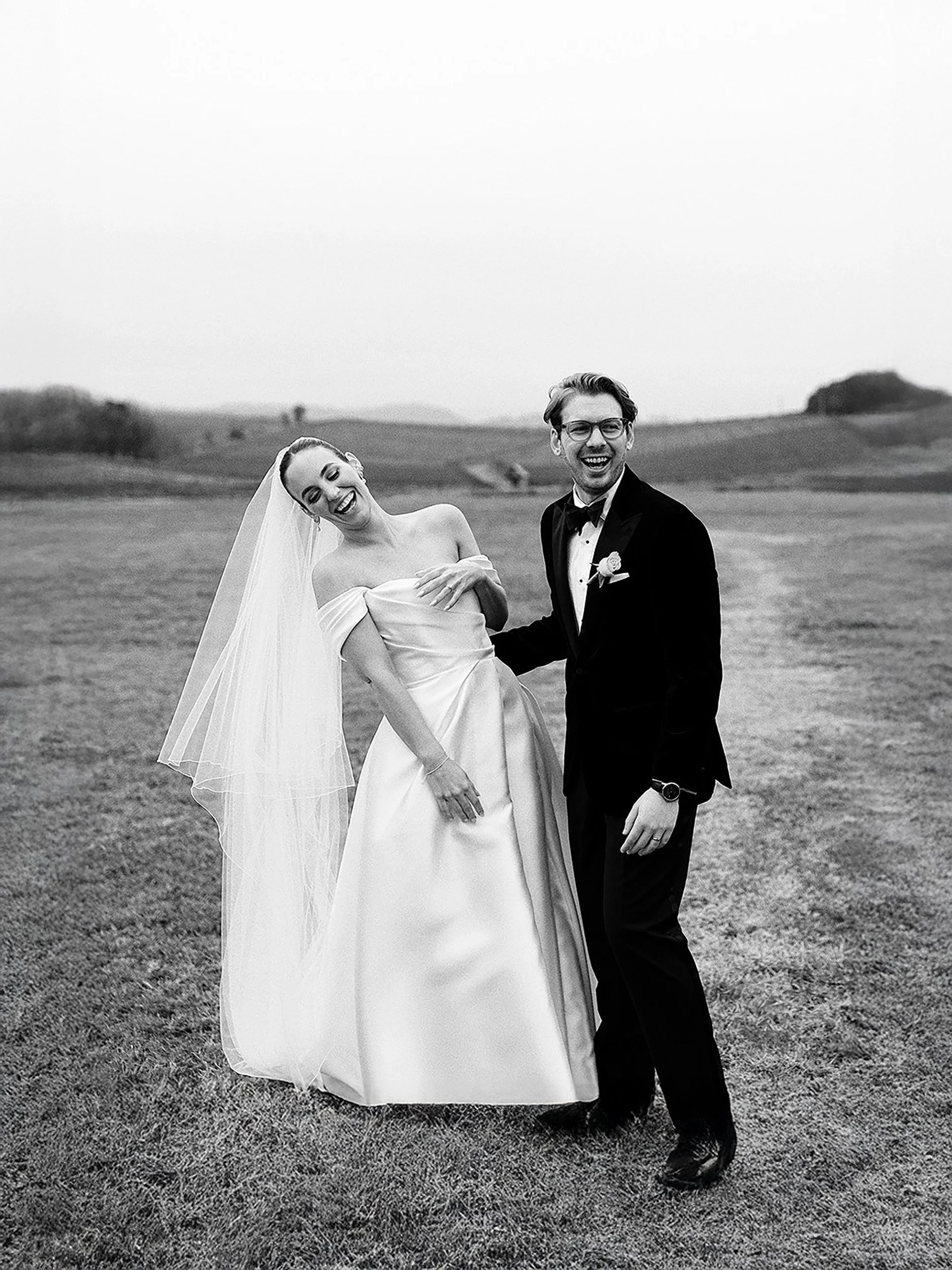 Bride and groom laughing together in an open field at Immerse in the Yarra Valley, candid black and white wedding portrait.