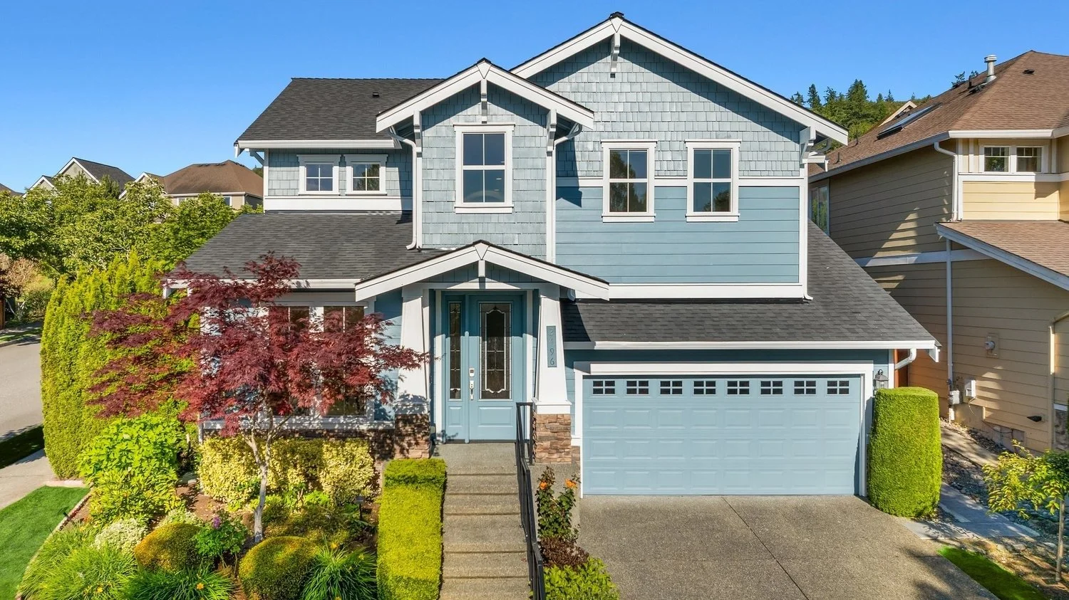 Beautiful blue two-story home with a garage, manicured landscaping, and bright sunny sky.