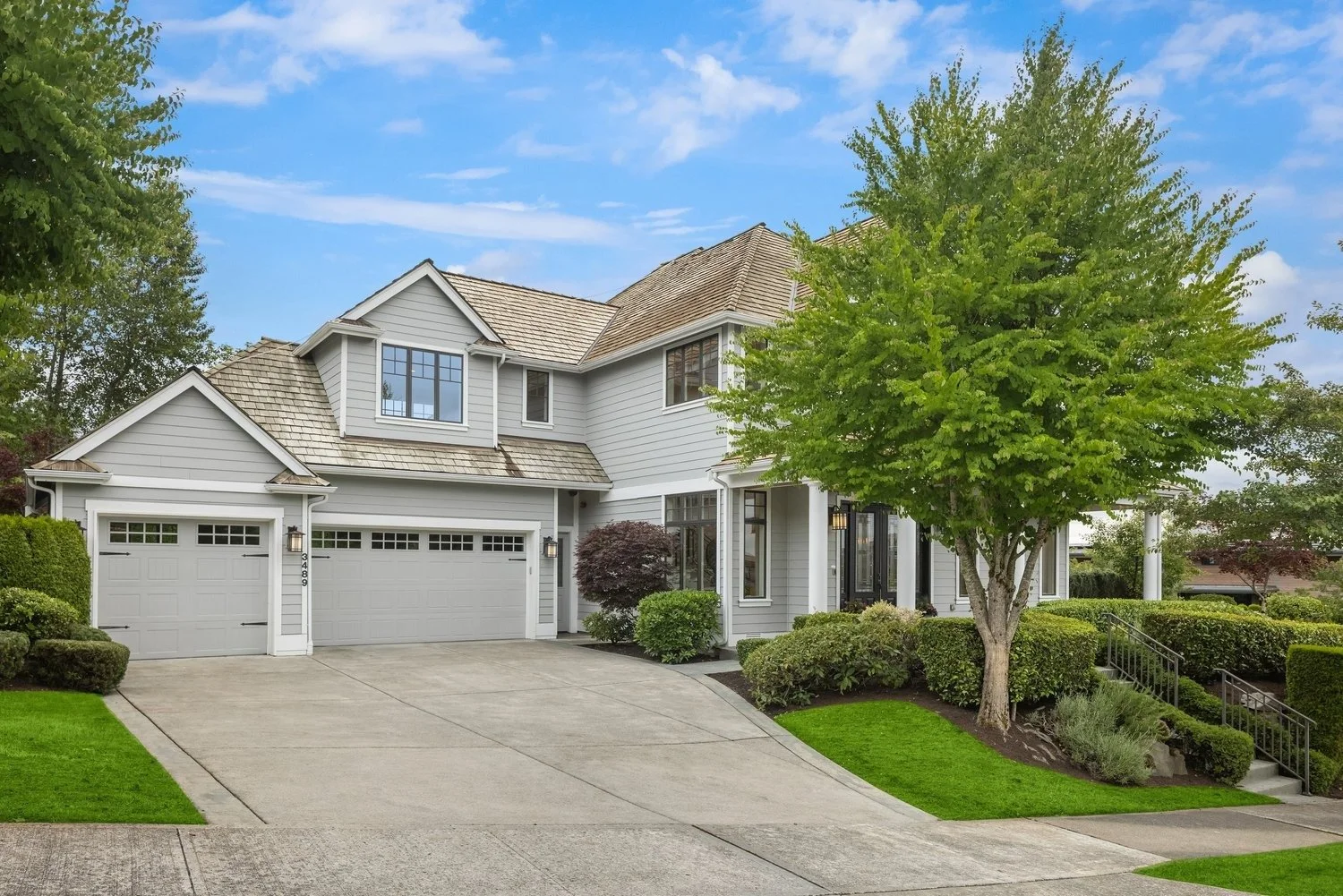 Modern two-story suburban home with landscaped yard, attached garage, driveway, trees, and bright blue sky.