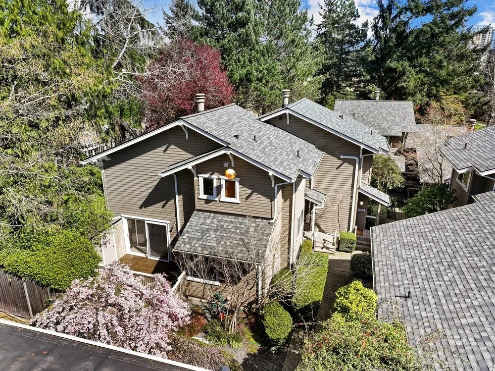 Aerial view of a charming residential neighborhood with gray-roofed homes, lush trees, gardens, and landscaped pathways.