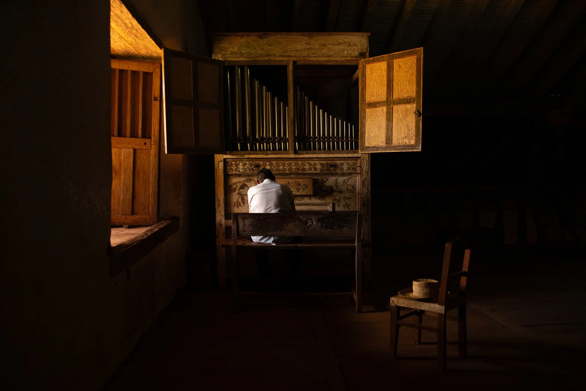 photo of a man sitting at an organ in a room dimly lit by orange light coming from a window