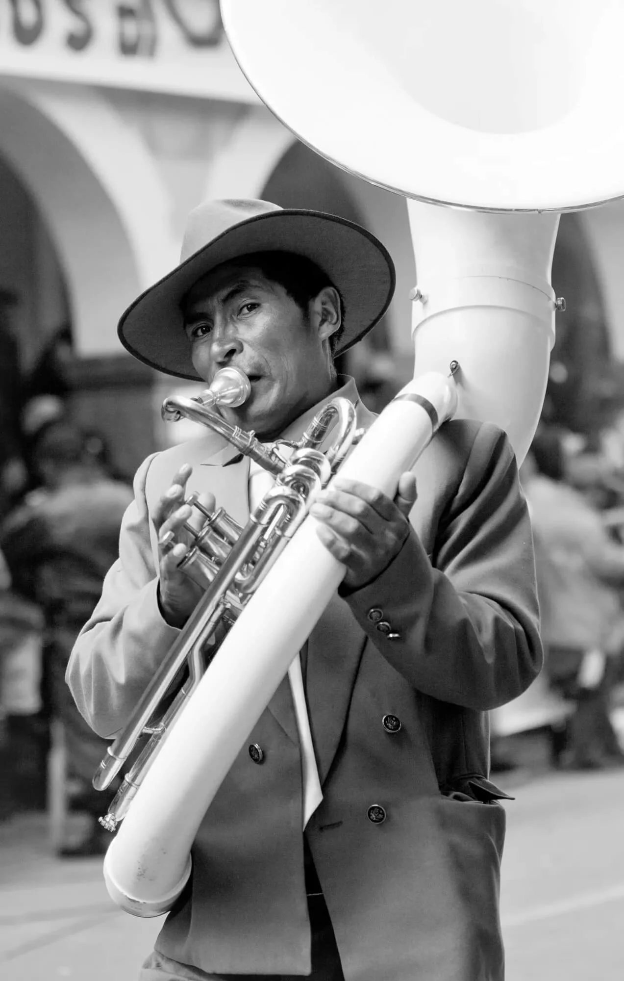 black and white photo portrait of a man in a suit and brimmed hat playing a white tuba for the Oruro Carnival