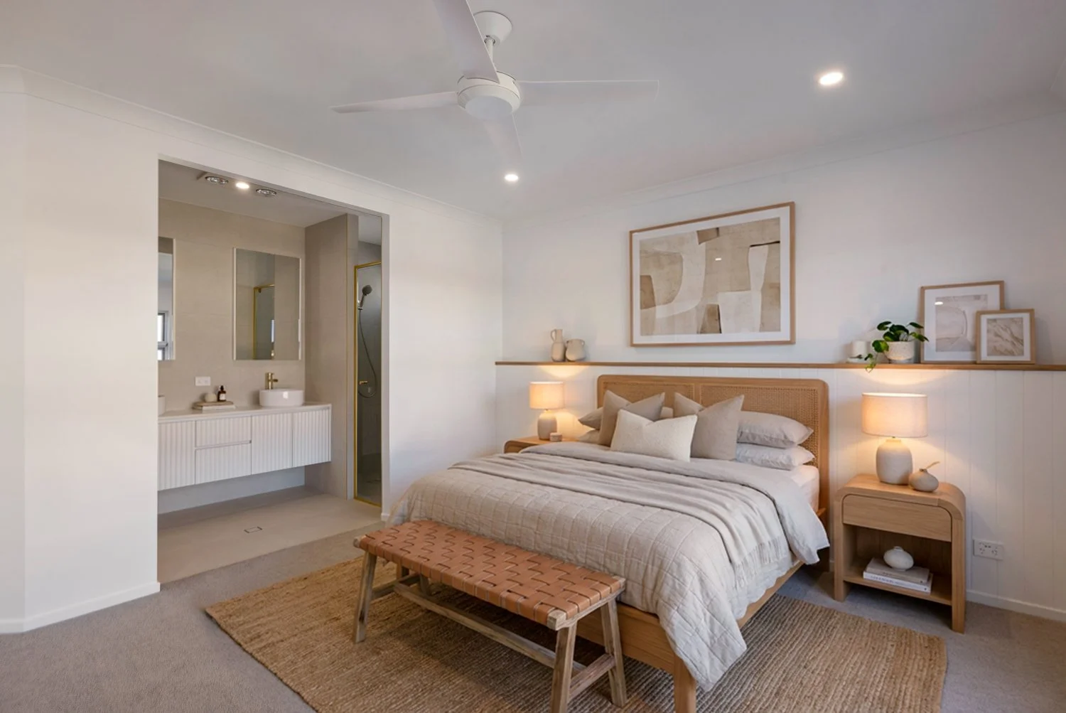 A cozy bedroom with a neatly made bed, neutral-colored bedding, and multiple pillows. There are two wooden nightstands with lamps on either side, framed artwork above the bed, and a woven bench at the foot of the bed. A small open shelf above the rig